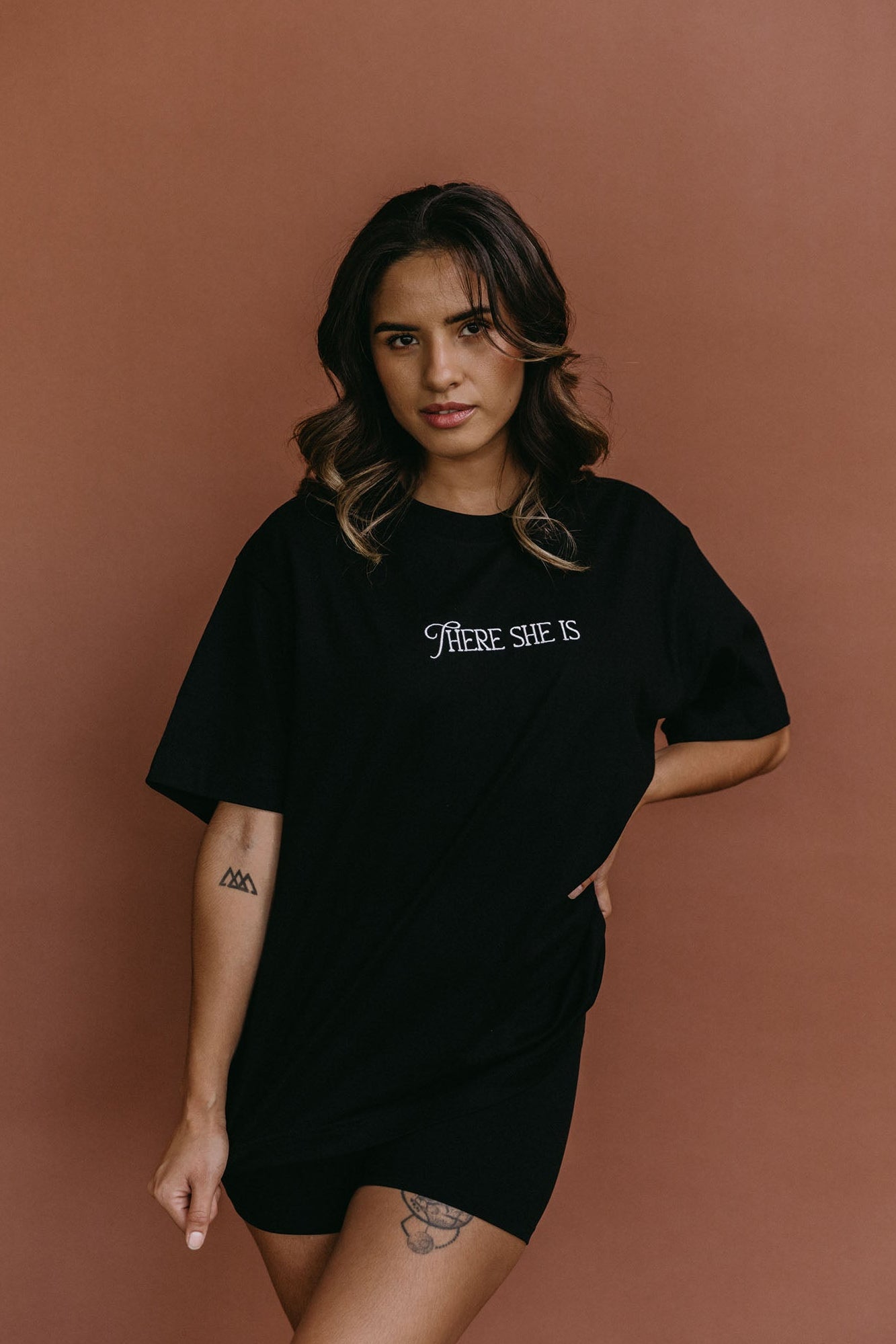 Female model wearing the black "There She Is" relaxed fit embroidered T-shirt by WNGSPN, styled with understated confidence.