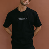 Male model wearing the black "There She Is" relaxed fit embroidered T-shirt by WNGSPN, styled with understated confidence.