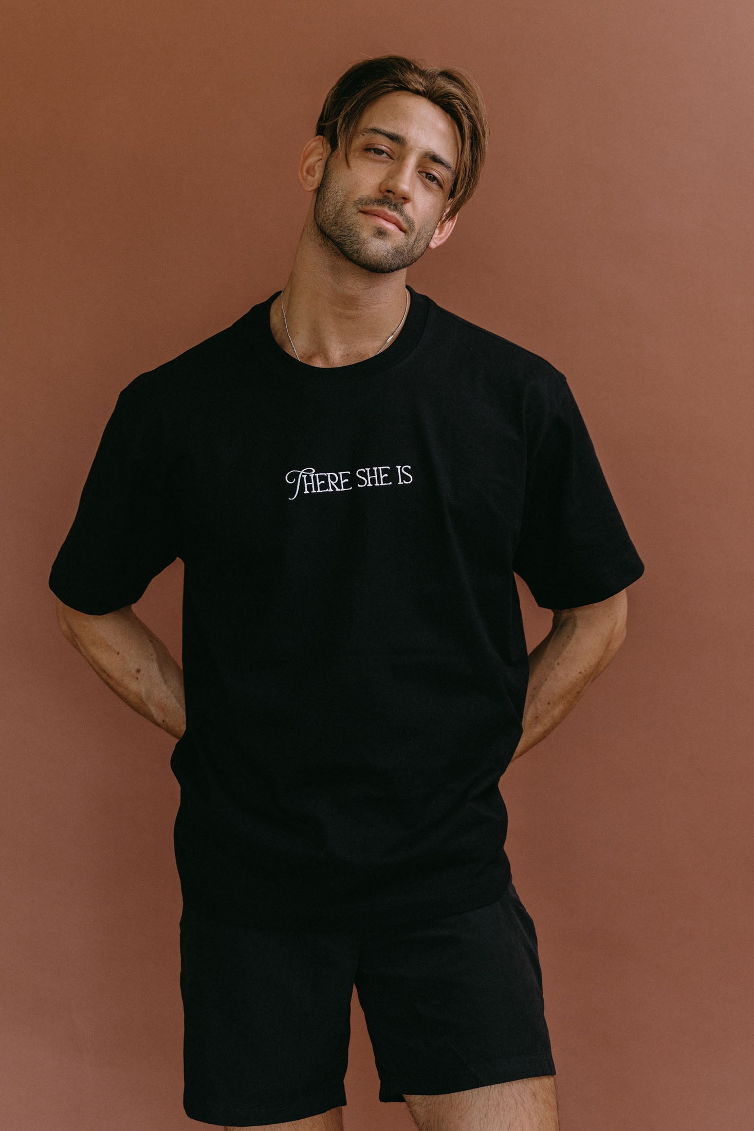 Male model wearing the black "There She Is" relaxed fit embroidered T-shirt by WNGSPN, styled with understated confidence.