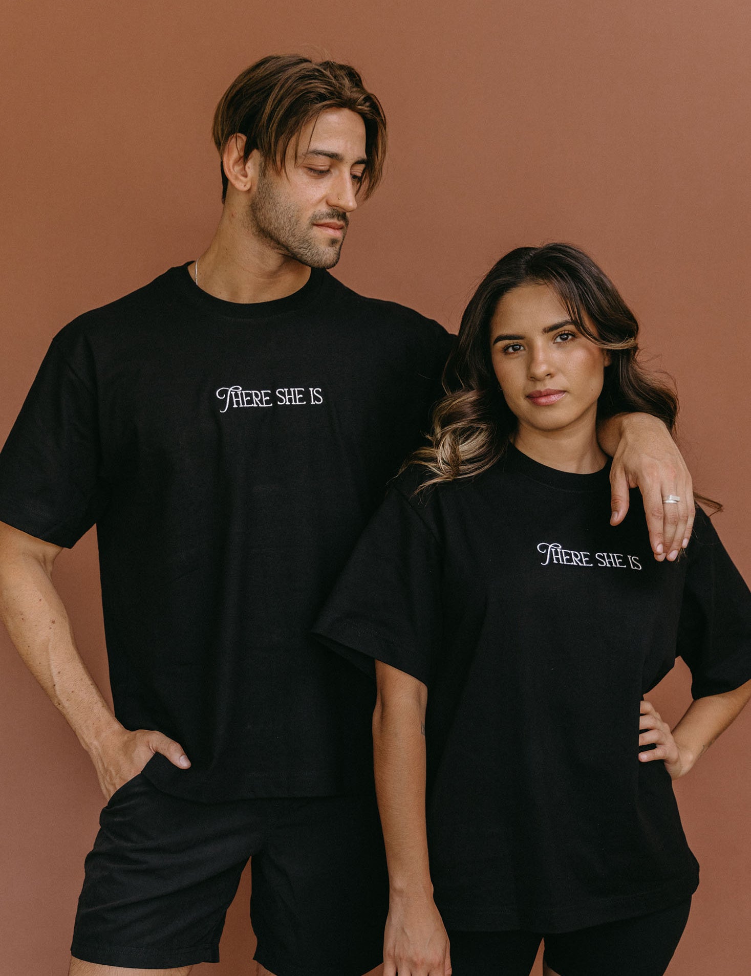 Couple wearing the black "There She Is" relaxed fit embroidered T-shirt by WNGSPN, styled as elevated romance reader apparel.