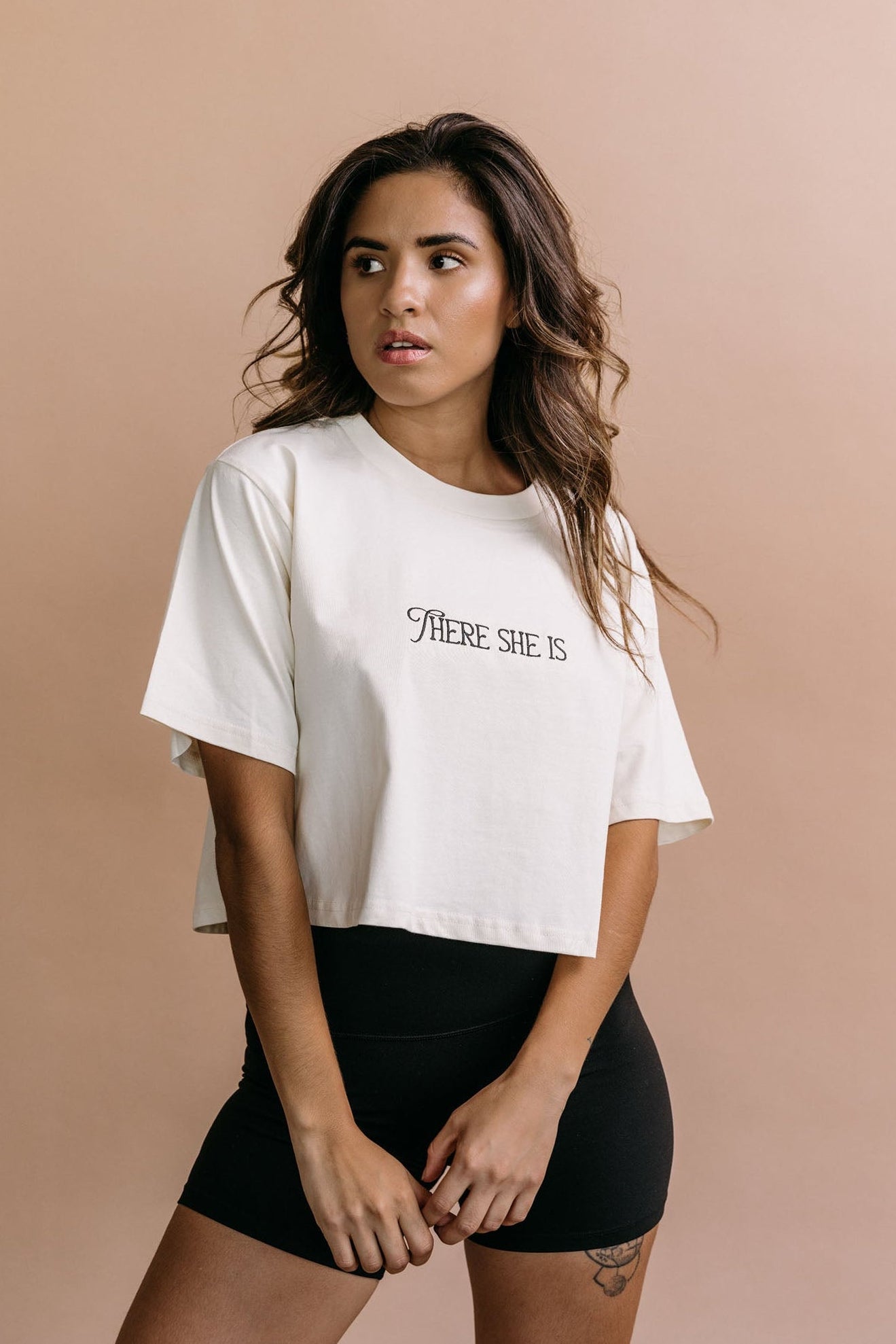 Female model wearing the ecru "There She Is" cropped embroidered T-shirt by WNGSPN, with a relaxed silhouette and clean lines.