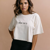 Female model wearing the ecru "There She Is" cropped embroidered T-shirt by WNGSPN, with a relaxed silhouette and clean lines.