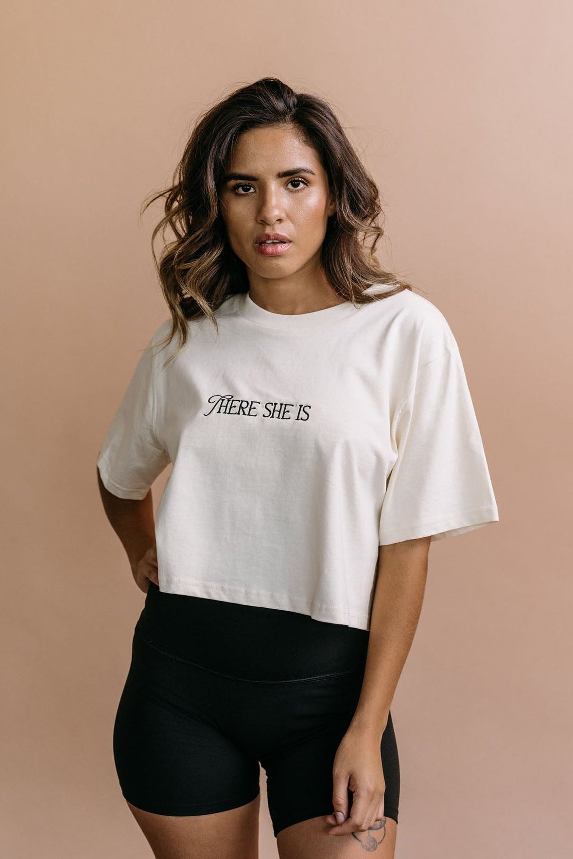 Female model wearing the ecru "There She Is" cropped embroidered T-shirt by WNGSPN, with a relaxed silhouette and clean lines.