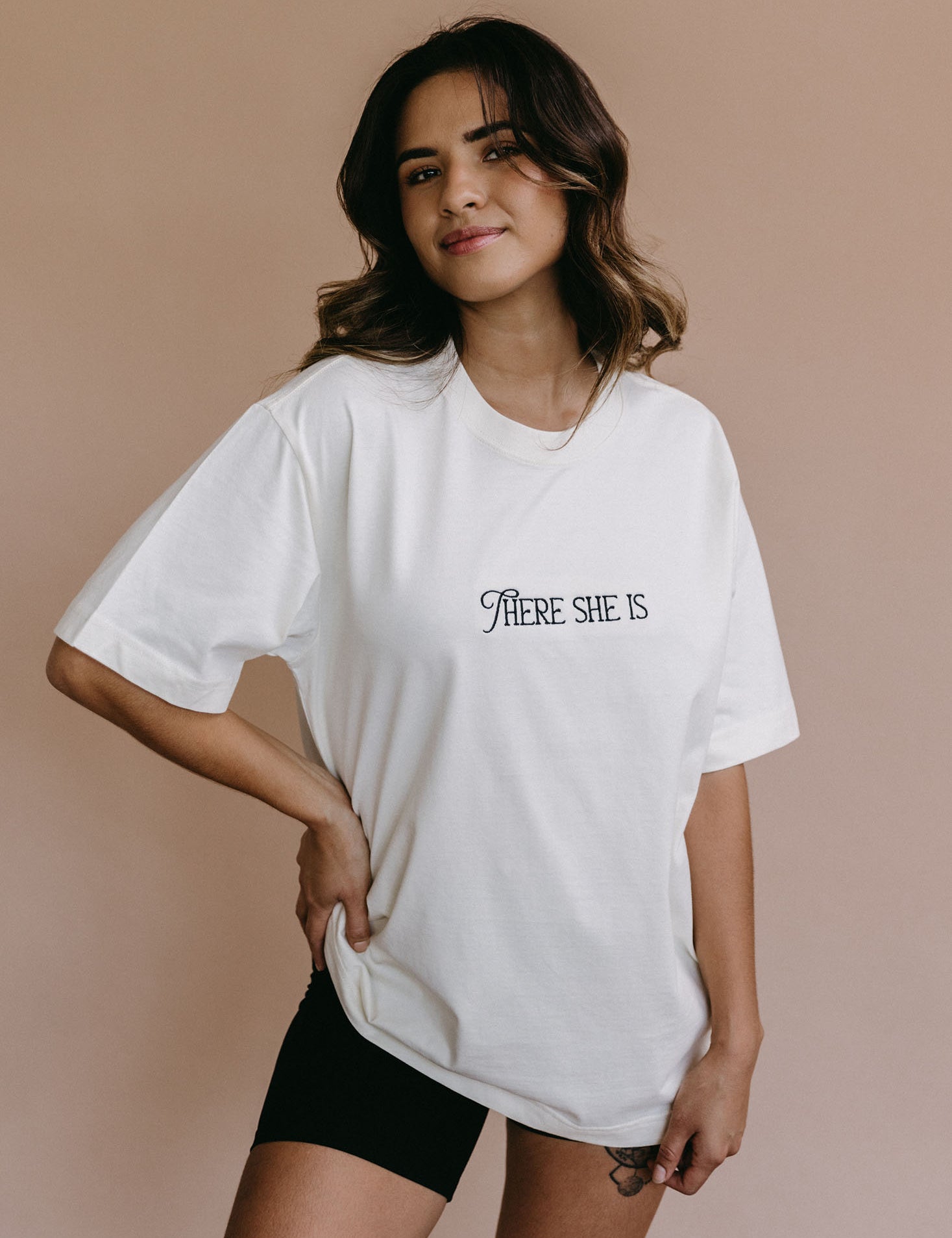 Female model wearing the ecru "There She Is" relaxed fit embroidered T-shirt by WNGSPN, styled in a minimal, elevated aesthetic.