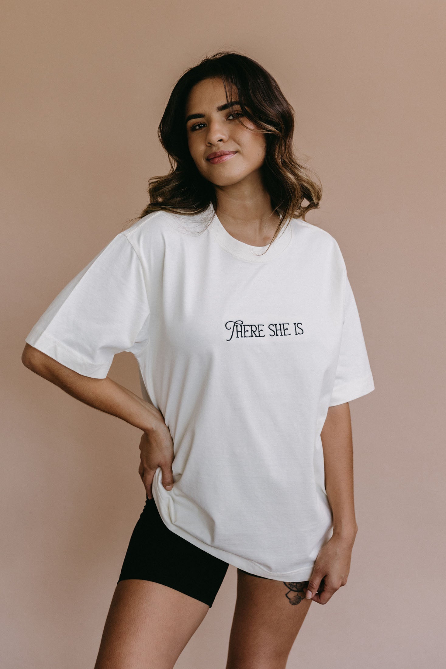 Female model wearing the ecru "There She Is" relaxed fit embroidered T-shirt by WNGSPN, styled in a minimal, elevated aesthetic.