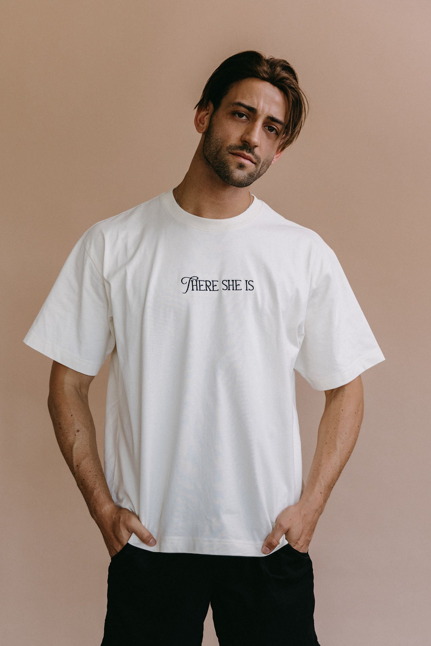 Male model wearing the ecru "There She Is" relaxed fit embroidered T-shirt by WNGSPN, styled in a minimal, elevated aesthetic.