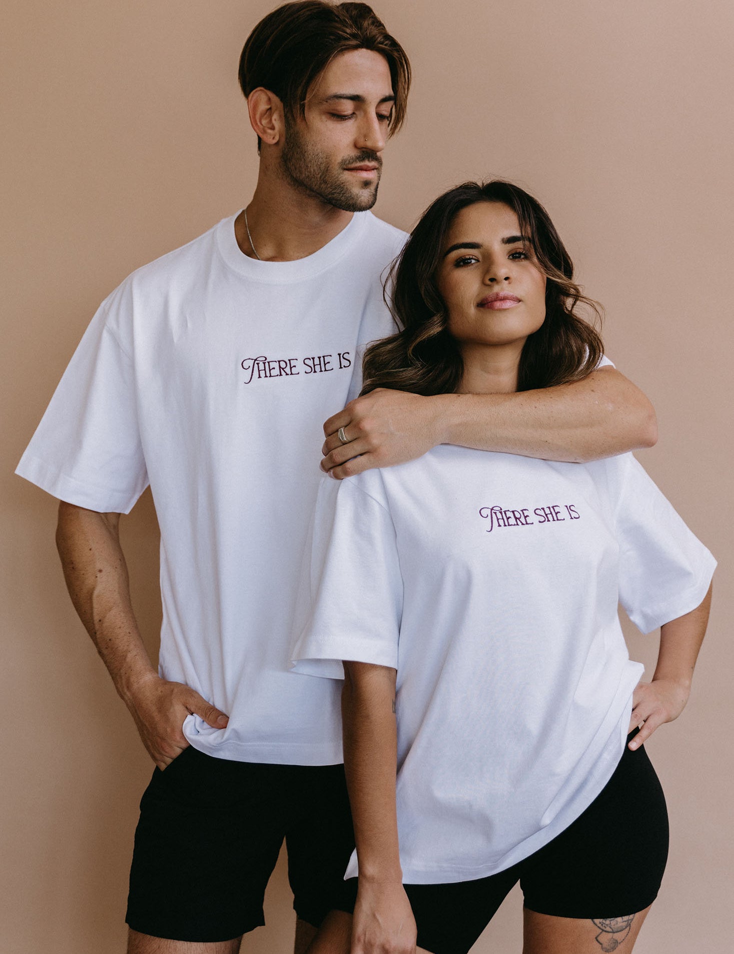 Couple wearing the white "There She Is" relaxed fit embroidered T-shirt by WNGSPN, with subtle tension and modern edge.