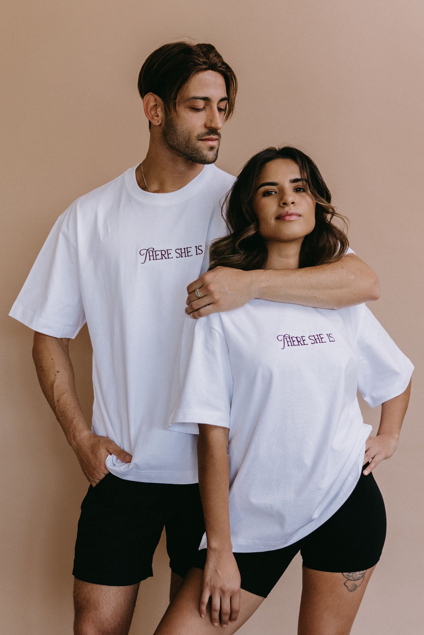 Couple wearing the white "There She Is" relaxed fit embroidered T-shirt by WNGSPN, with subtle tension and modern edge.