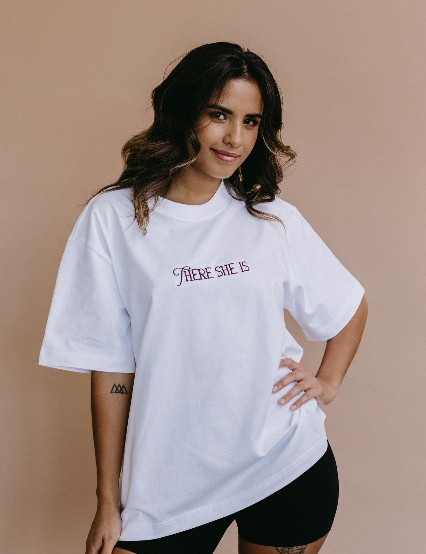 Female model wearing the white "There She Is" relaxed fit embroidered T-shirt by WNGSPN, with a relaxed silhouette and clean lines.