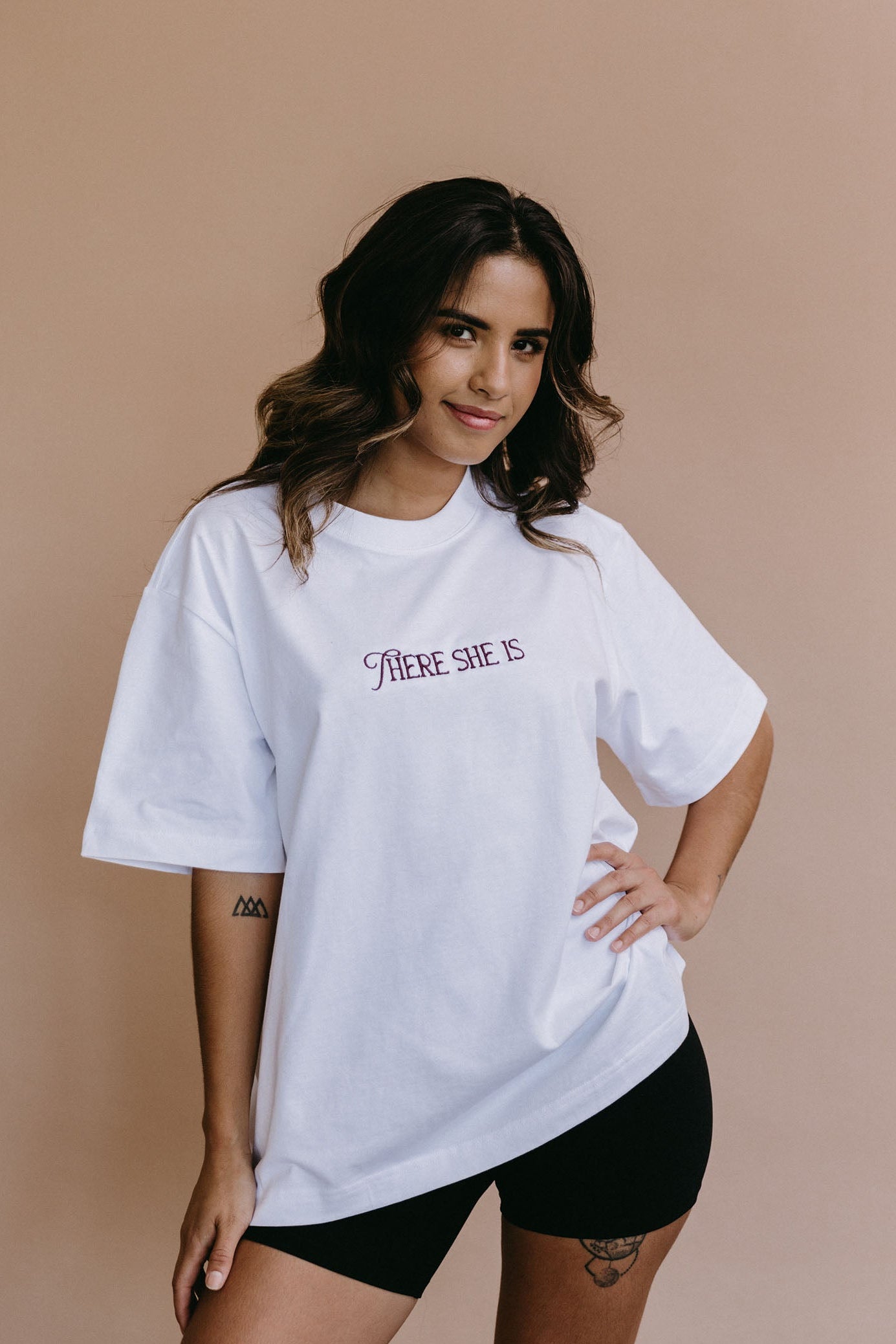 Female model wearing the white "There She Is" relaxed fit embroidered T-shirt by WNGSPN, with a relaxed silhouette and clean lines.