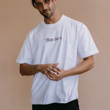 Male model wearing the white "There She Is" relaxed fit embroidered T-shirt by WNGSPN, with a relaxed silhouette and clean lines.
