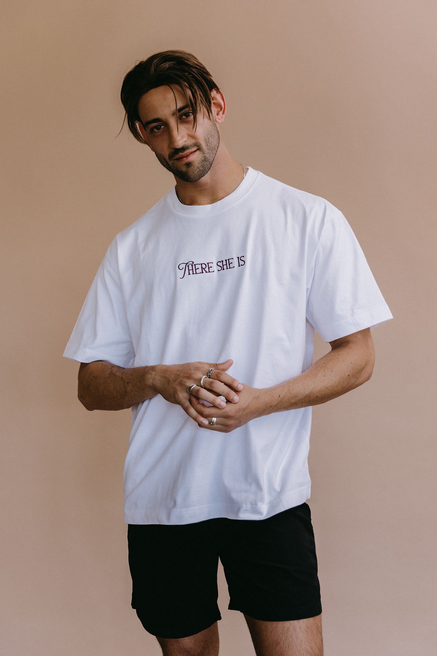 Male model wearing the white "There She Is" relaxed fit embroidered T-shirt by WNGSPN, with a relaxed silhouette and clean lines.