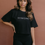Female model wearing the black "Use Your Words" cropped embroidered T-shirt by WNGSPN, styled with understated confidence.