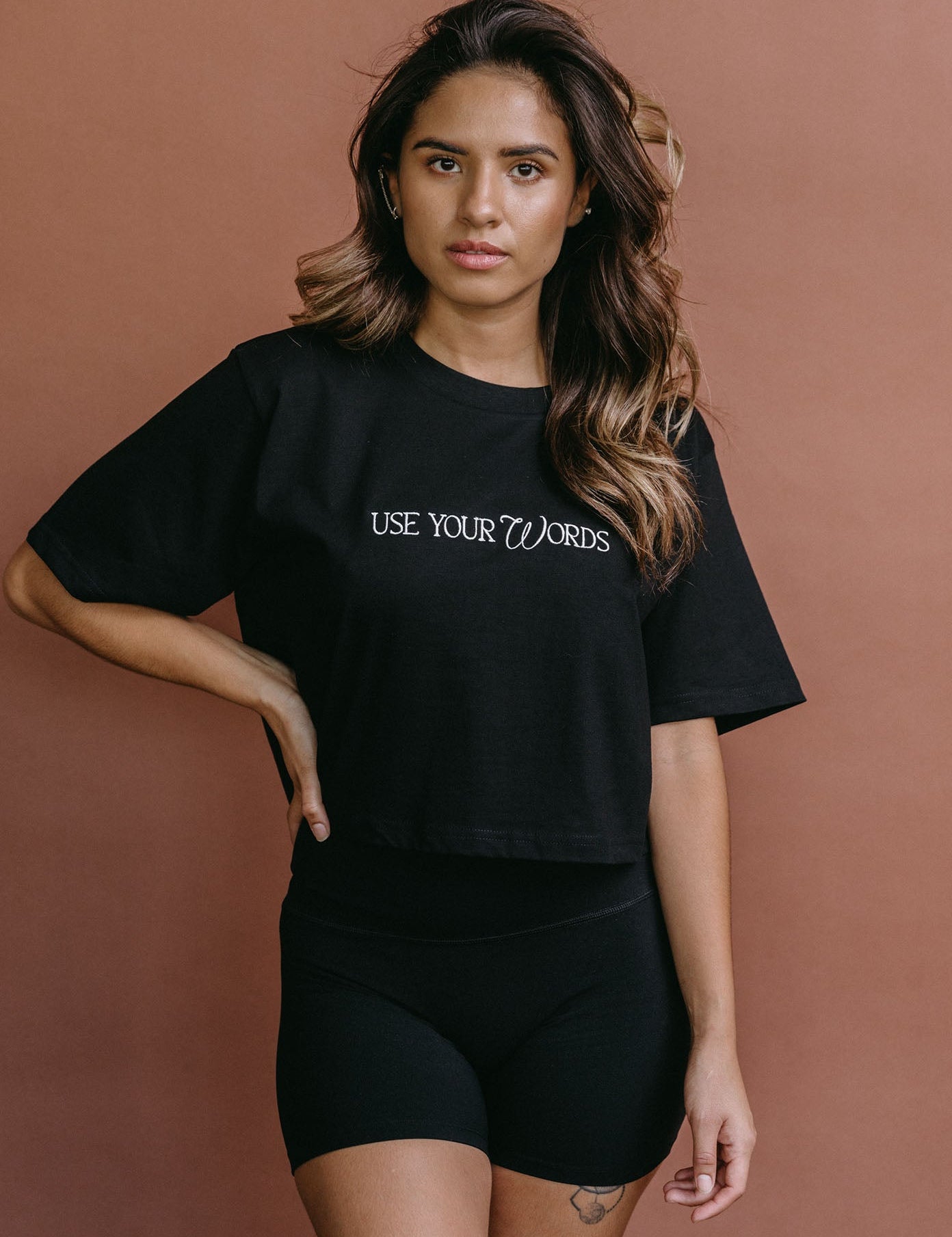 Female model wearing the black "Use Your Words" cropped embroidered T-shirt by WNGSPN, styled with understated confidence.