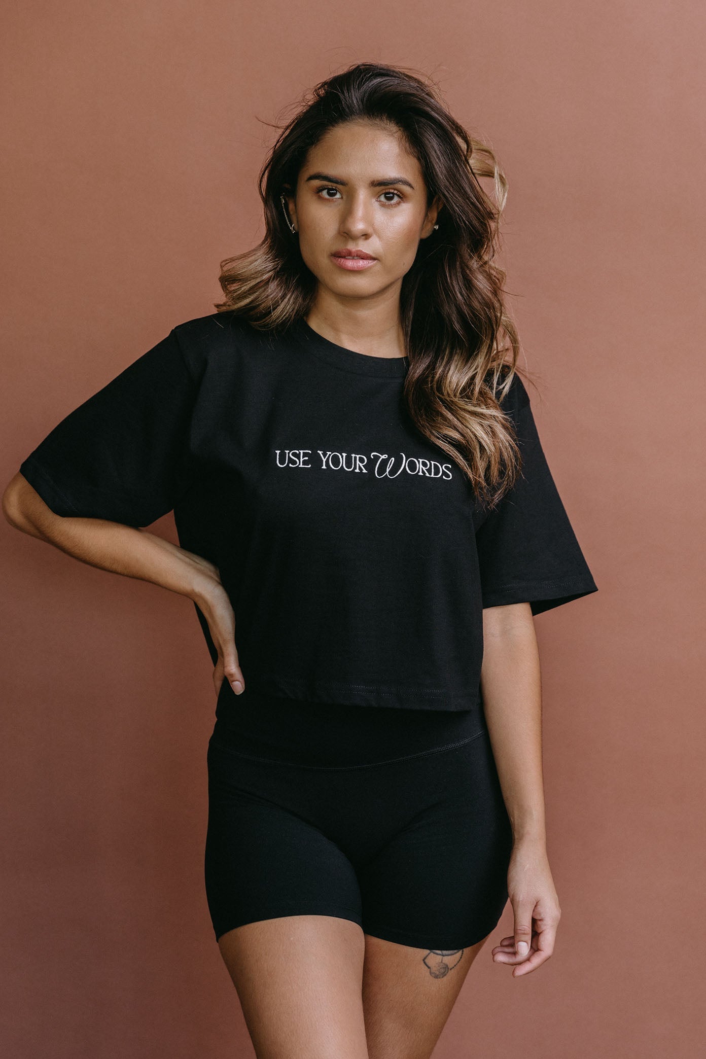Female model wearing the black "Use Your Words" cropped embroidered T-shirt by WNGSPN, styled with understated confidence.