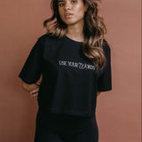 Female model wearing the black "Use Your Words" cropped embroidered T-shirt by WNGSPN, with a relaxed silhouette and clean lines.
