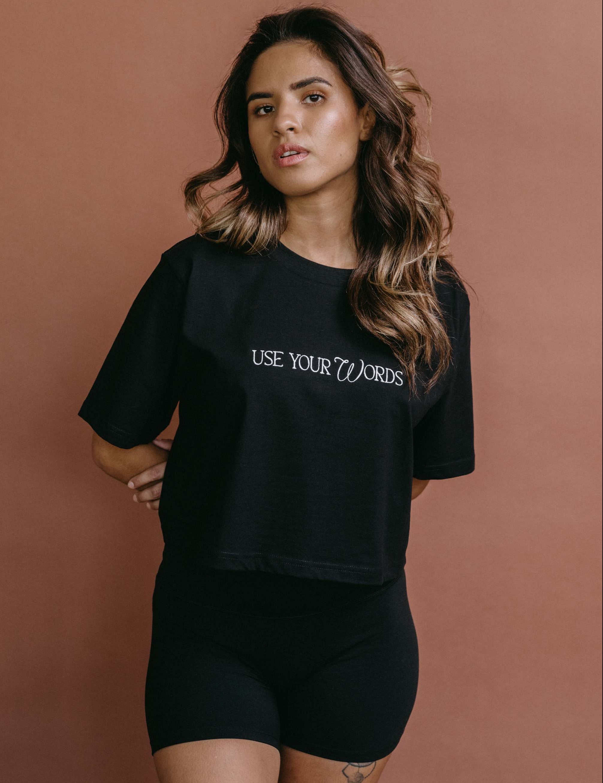 Female model wearing the black "Use Your Words" cropped embroidered T-shirt by WNGSPN, with a relaxed silhouette and clean lines.
