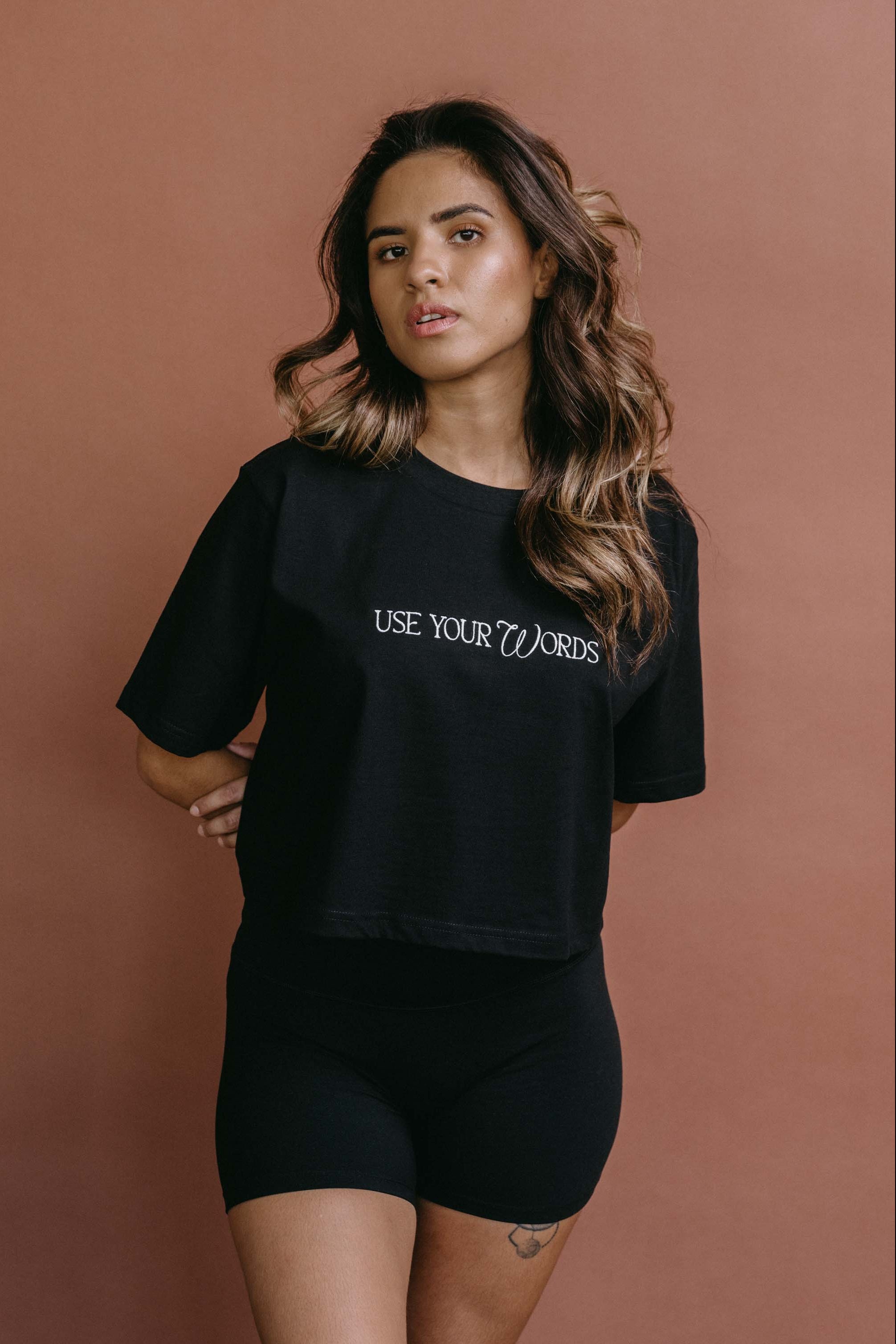 Female model wearing the black "Use Your Words" cropped embroidered T-shirt by WNGSPN, with a relaxed silhouette and clean lines.