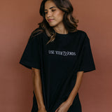 Female model wearing the black "Use Your Words" relaxed fit embroidered T-shirt by WNGSPN, styled with understated confidence.