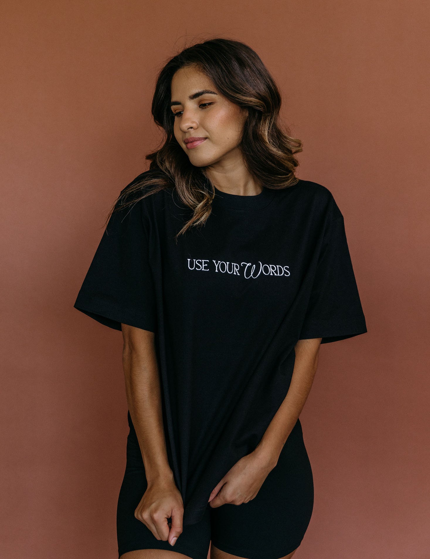 Female model wearing the black "Use Your Words" relaxed fit embroidered T-shirt by WNGSPN, styled with understated confidence.