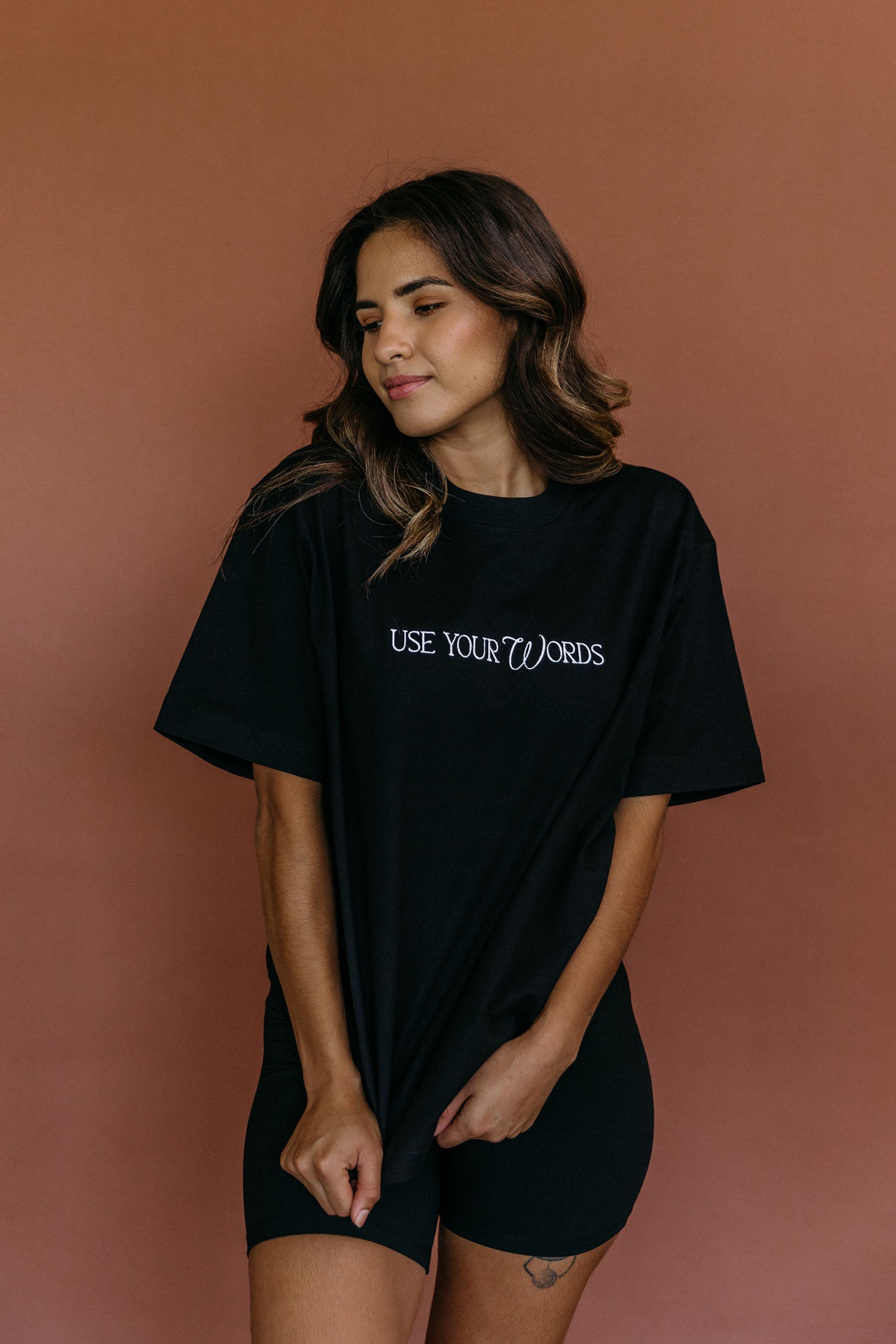 Female model wearing the black "Use Your Words" relaxed fit embroidered T-shirt by WNGSPN, styled with understated confidence.
