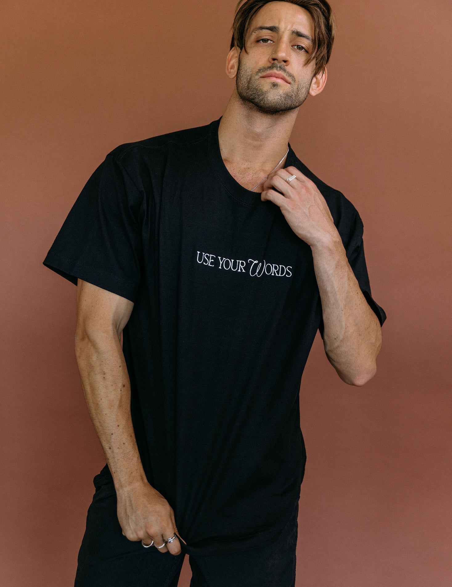 Male model wearing the black "Use Your Words" relaxed fit embroidered T-shirt by WNGSPN, styled with understated confidence.