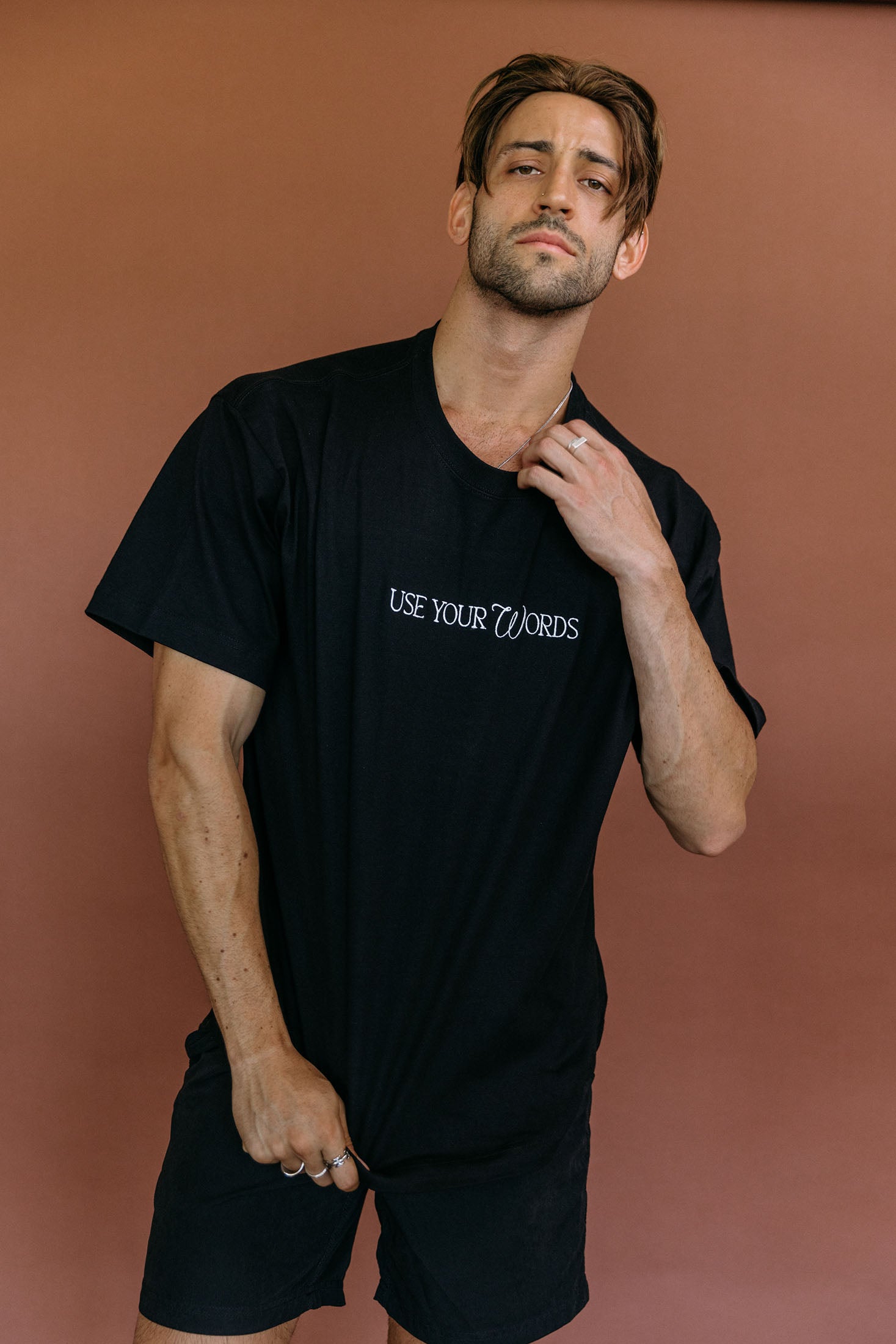 Male model wearing the black "Use Your Words" relaxed fit embroidered T-shirt by WNGSPN, styled with understated confidence.