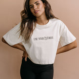 Female model wearing the ecru "Use Your Words" cropped embroidered T-shirt by WNGSPN, with a relaxed silhouette and clean lines.
