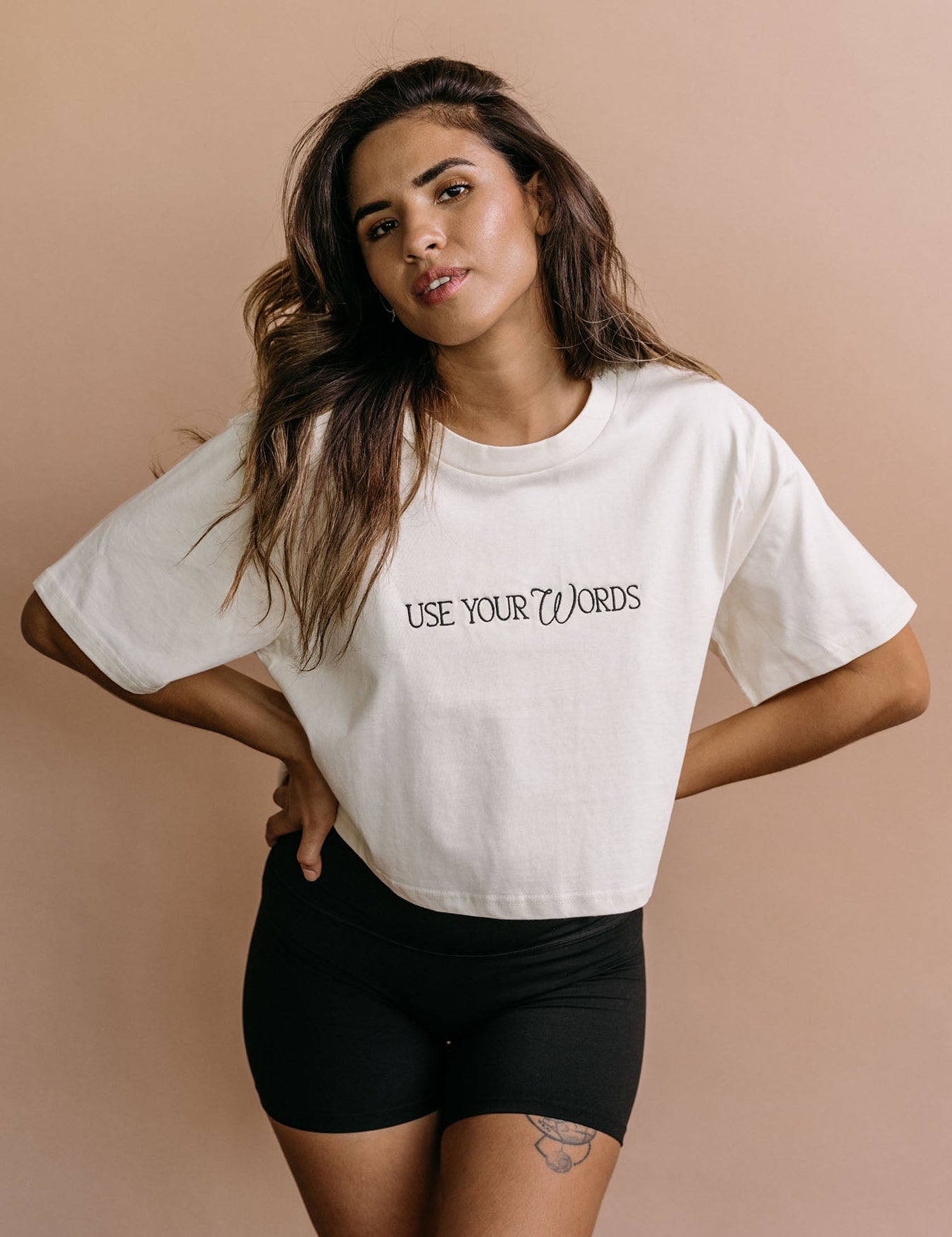 Female model wearing the ecru "Use Your Words" cropped embroidered T-shirt by WNGSPN, with a relaxed silhouette and clean lines.