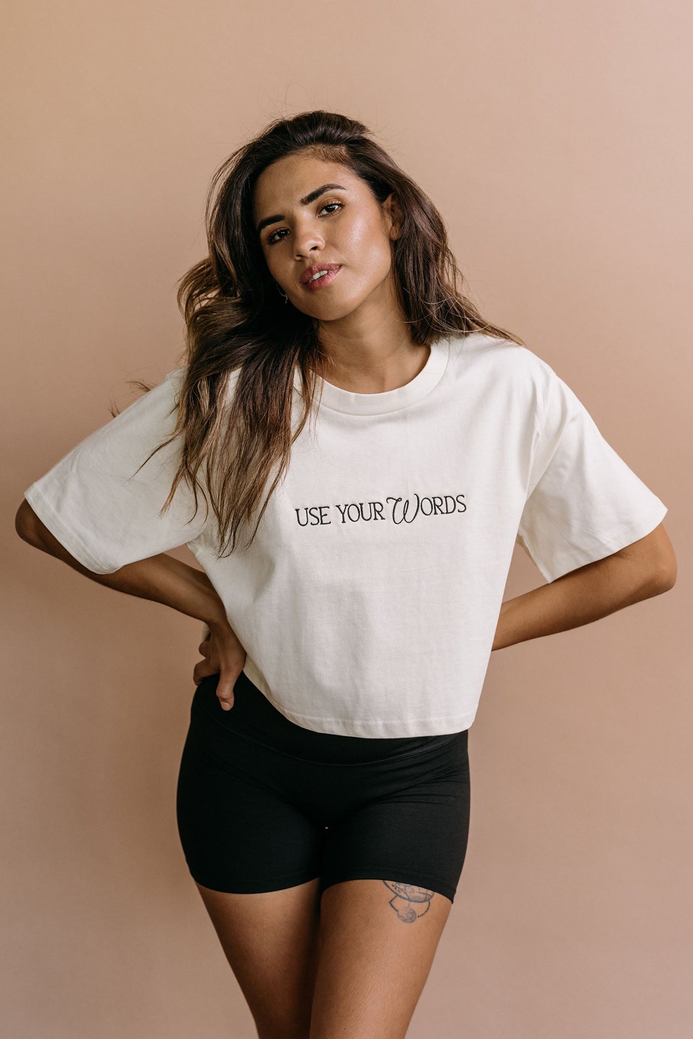 Female model wearing the ecru "Use Your Words" cropped embroidered T-shirt by WNGSPN, with a relaxed silhouette and clean lines.