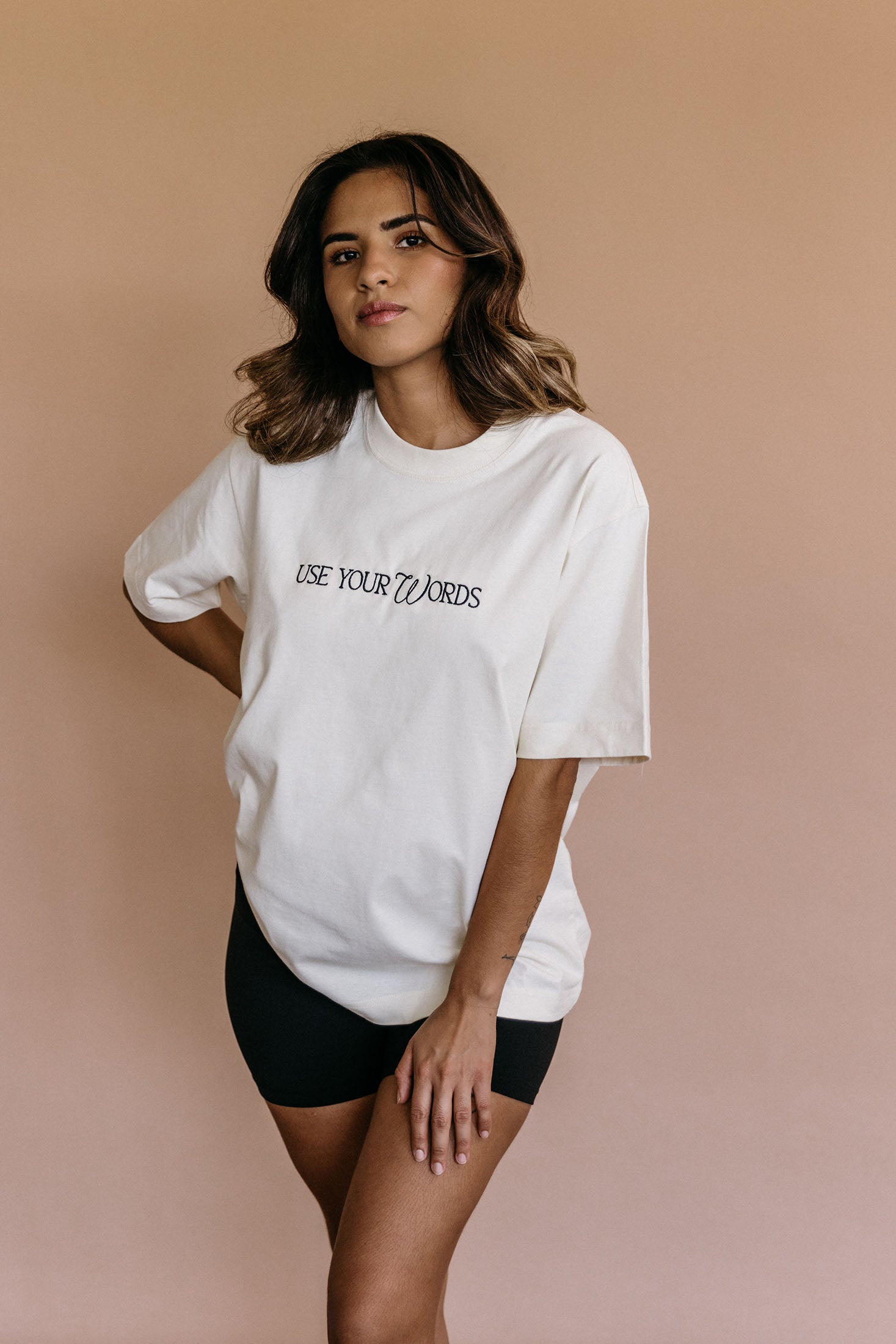 Female model wearing the ecru "Use Your Words" relaxed fit embroidered T-shirt by WNGSPN, styled in a minimal, elevated aesthetic.