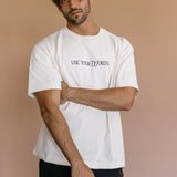 Male model wearing the ecru "Use Your Words" relaxed fit embroidered T-shirt by WNGSPN, styled in a minimal, elevated aesthetic.