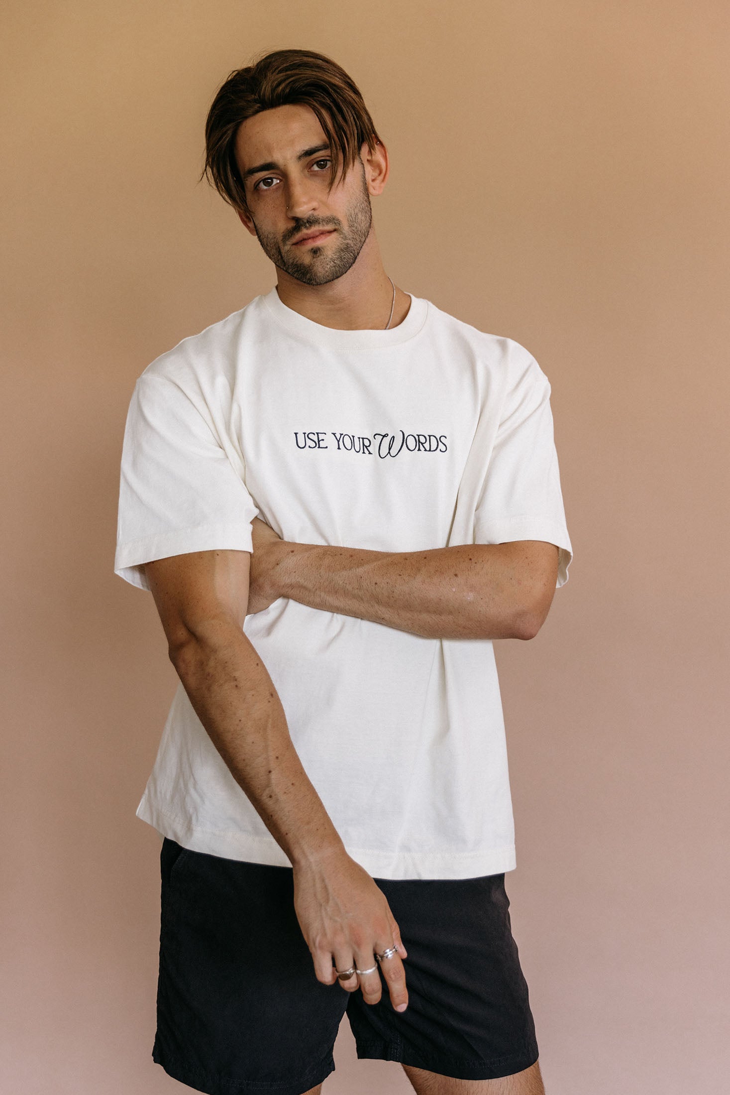 Male model wearing the ecru "Use Your Words" relaxed fit embroidered T-shirt by WNGSPN, styled in a minimal, elevated aesthetic.