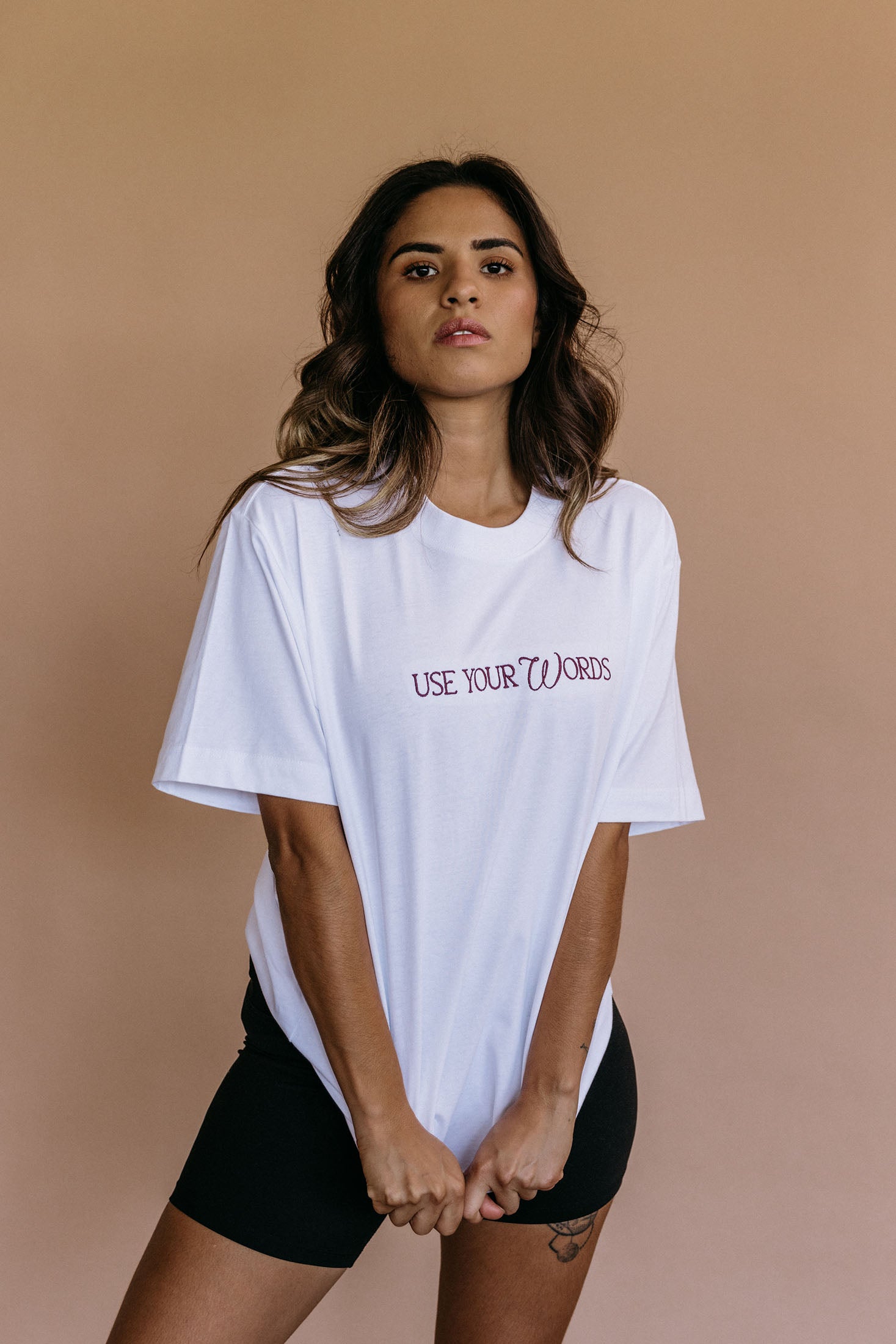 Female model wearing the white "Use Your Words" relaxed fit embroidered T-shirt by WNGSPN, with a relaxed silhouette and clean lines.