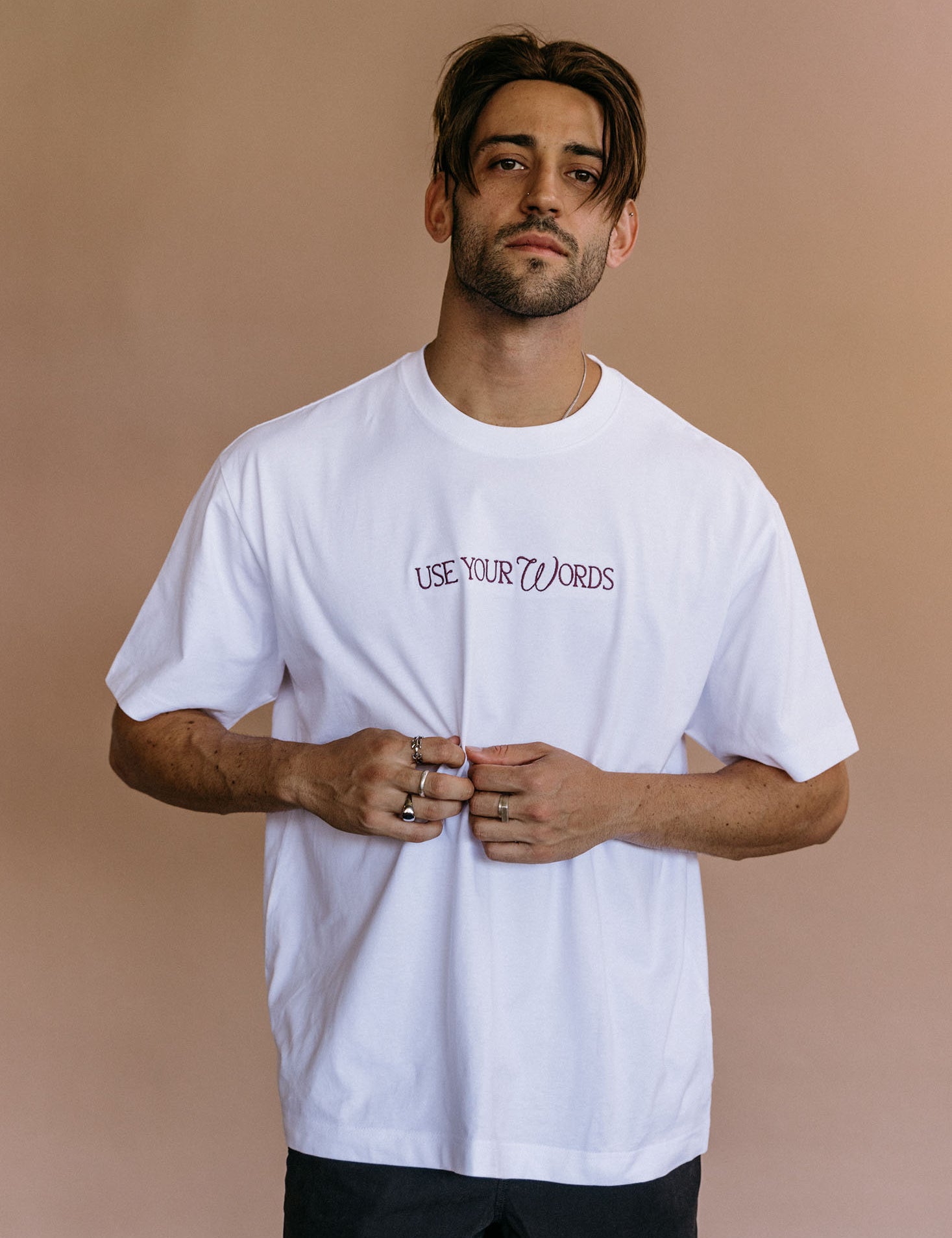Male model wearing the white "Use Your Words" relaxed fit embroidered T-shirt by WNGSPN, with a relaxed silhouette and clean lines.