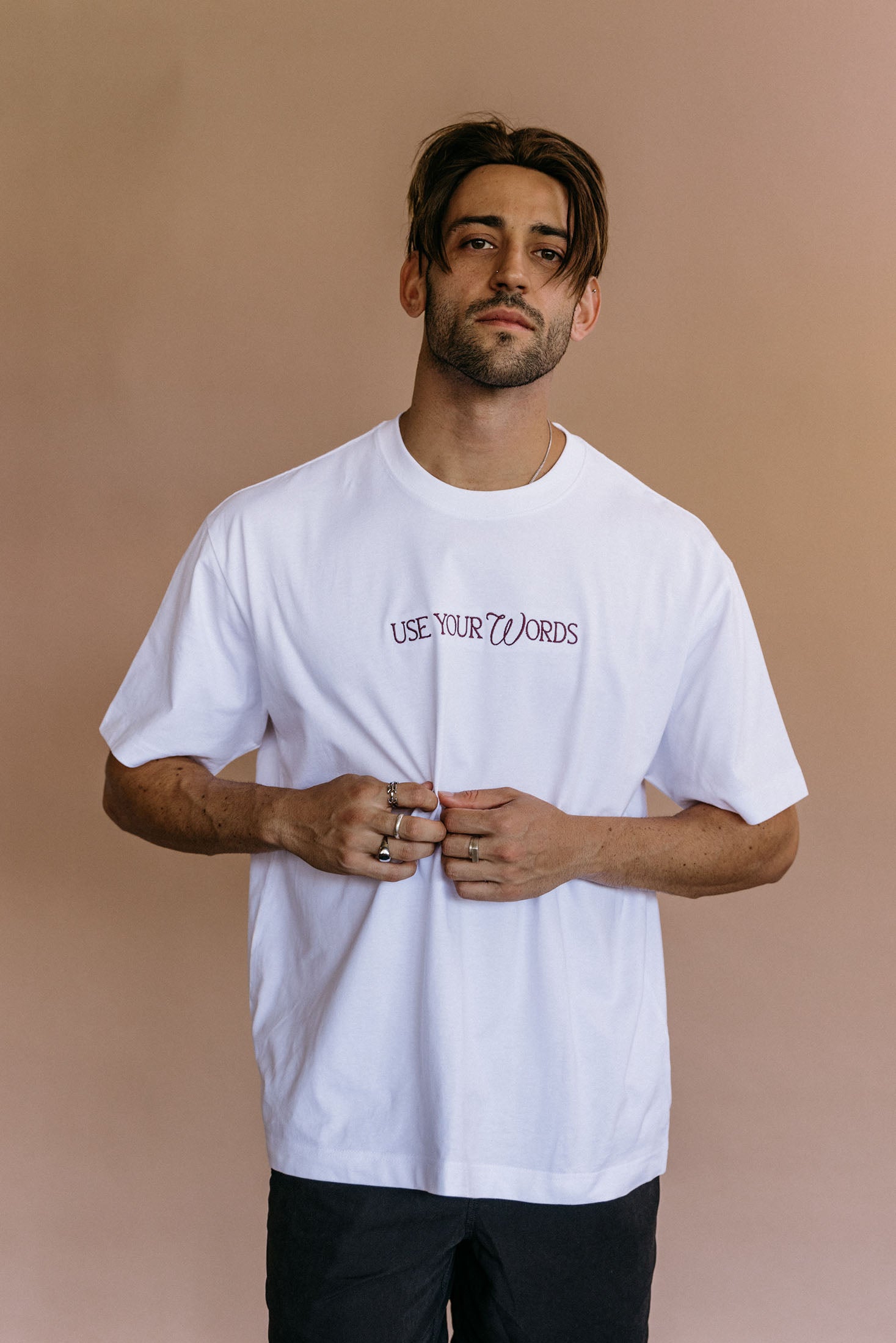 Male model wearing the white "Use Your Words" relaxed fit embroidered T-shirt by WNGSPN, with a relaxed silhouette and clean lines.