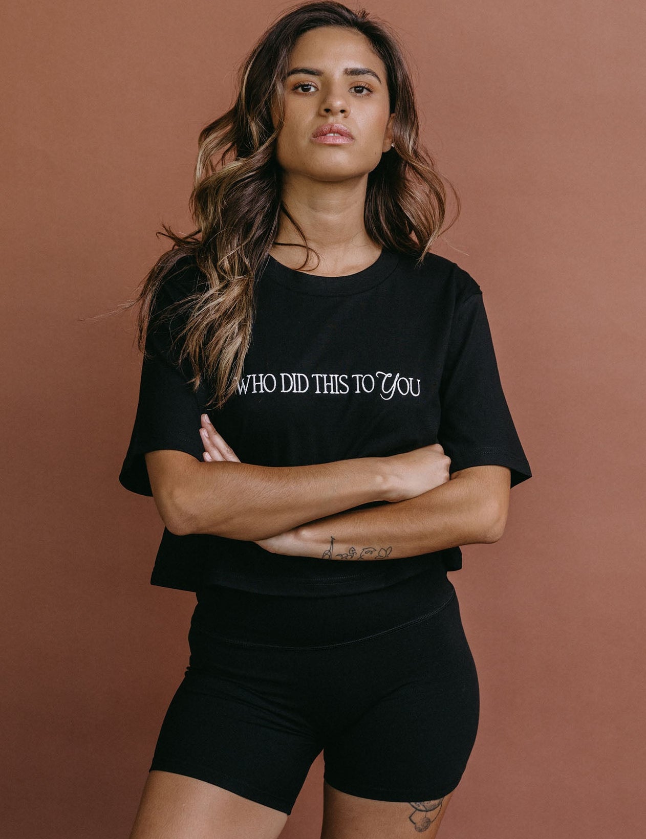 Female model wearing the black "Who Did This To You" cropped embroidered T-shirt by WNGSPN, styled with understated confidence.
