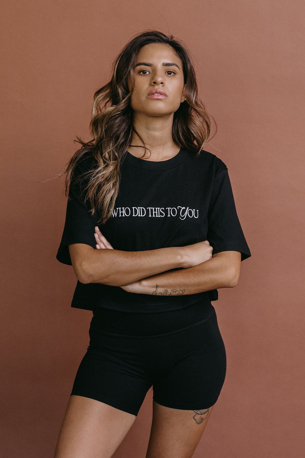 Female model wearing the black "Who Did This To You" cropped embroidered T-shirt by WNGSPN, styled with understated confidence.
