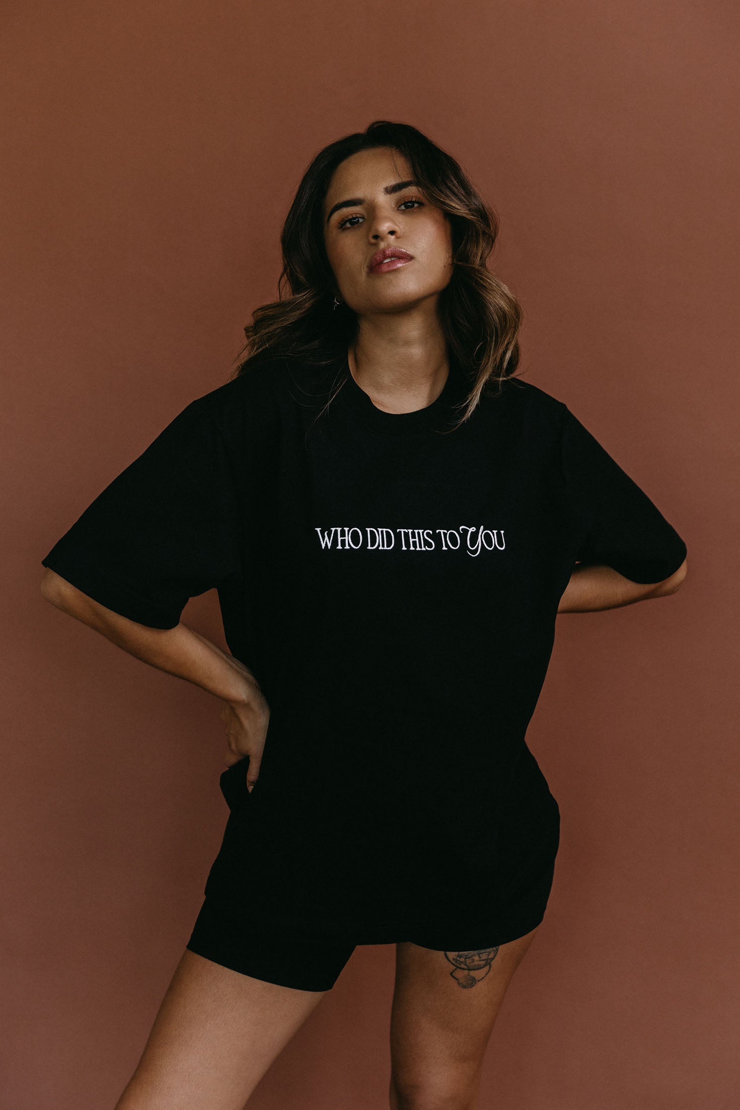 Female model wearing the black "Who Did This To You" relaxed fit embroidered T-shirt by WNGSPN, styled with understated confidence.