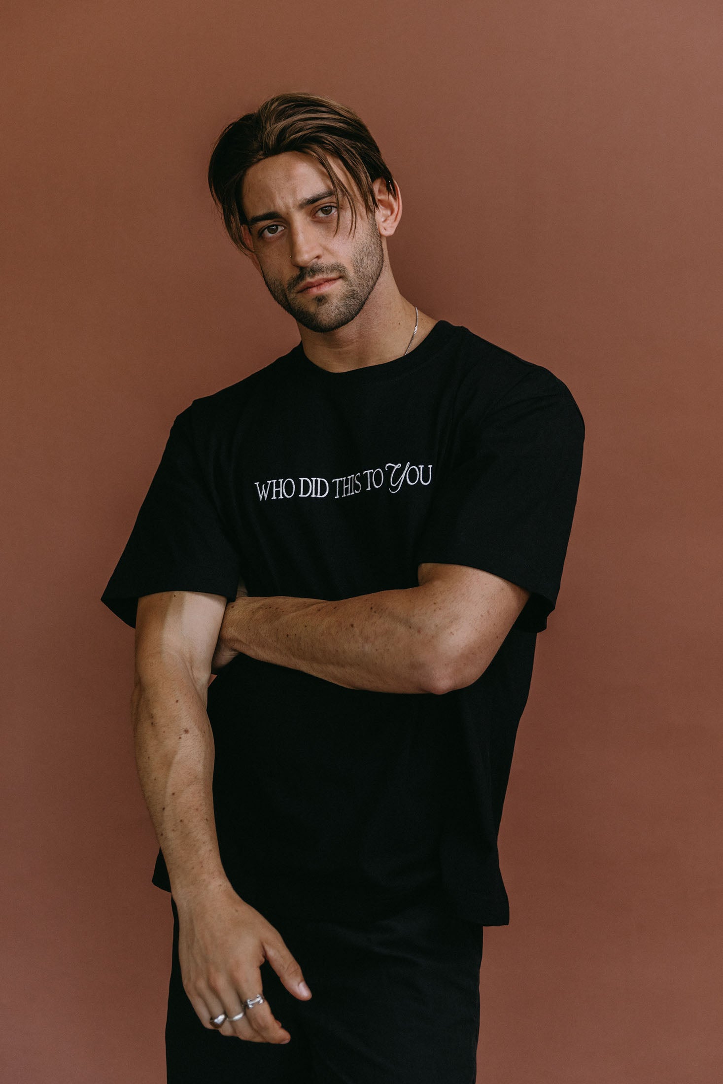 Male model wearing the black "Who Did This To You" relaxed fit embroidered T-shirt by WNGSPN, styled with understated confidence.
