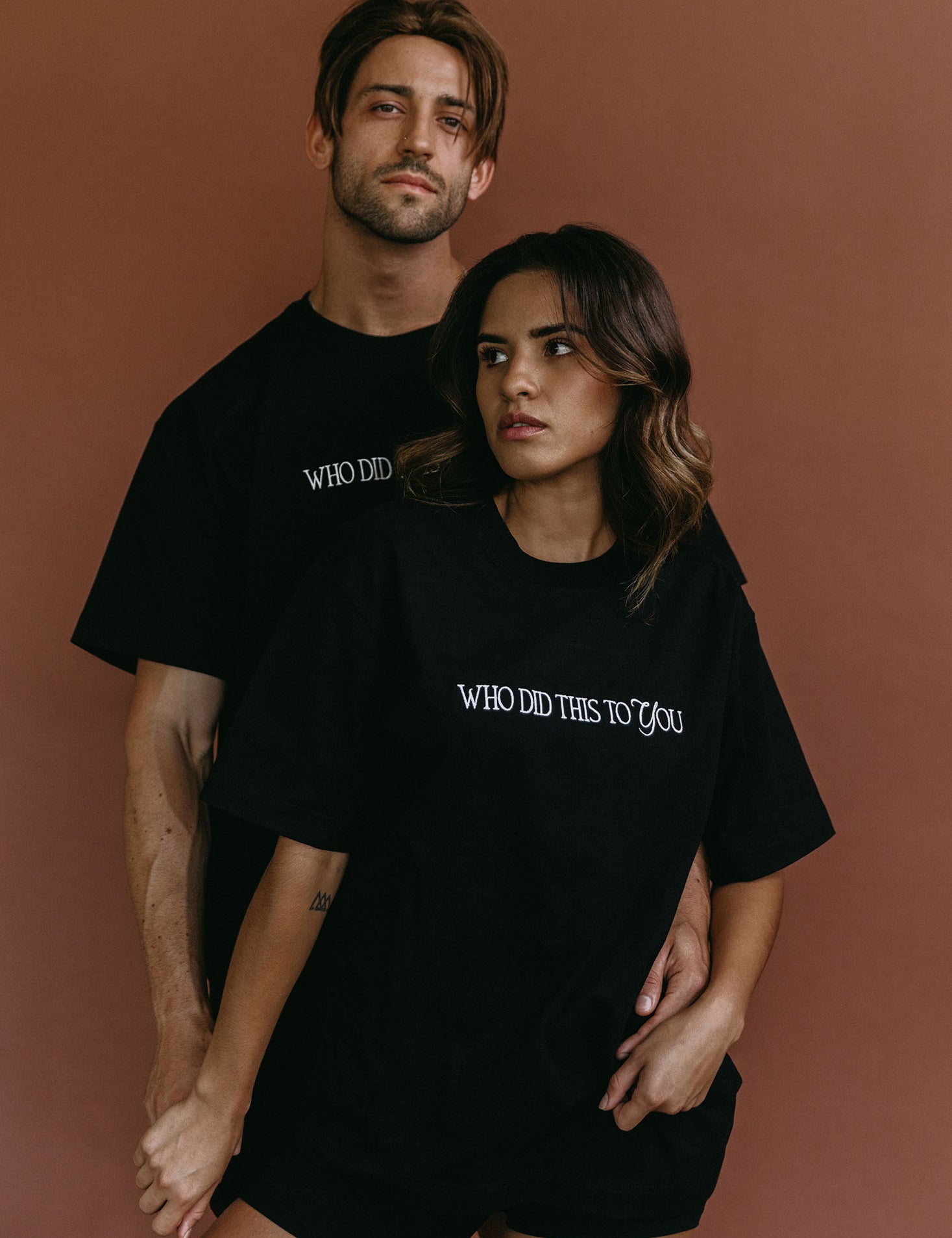Couple wearing the black "Who Did This To You" relaxed fit embroidered T-shirt by WNGSPN, styled as elevated romance reader apparel.