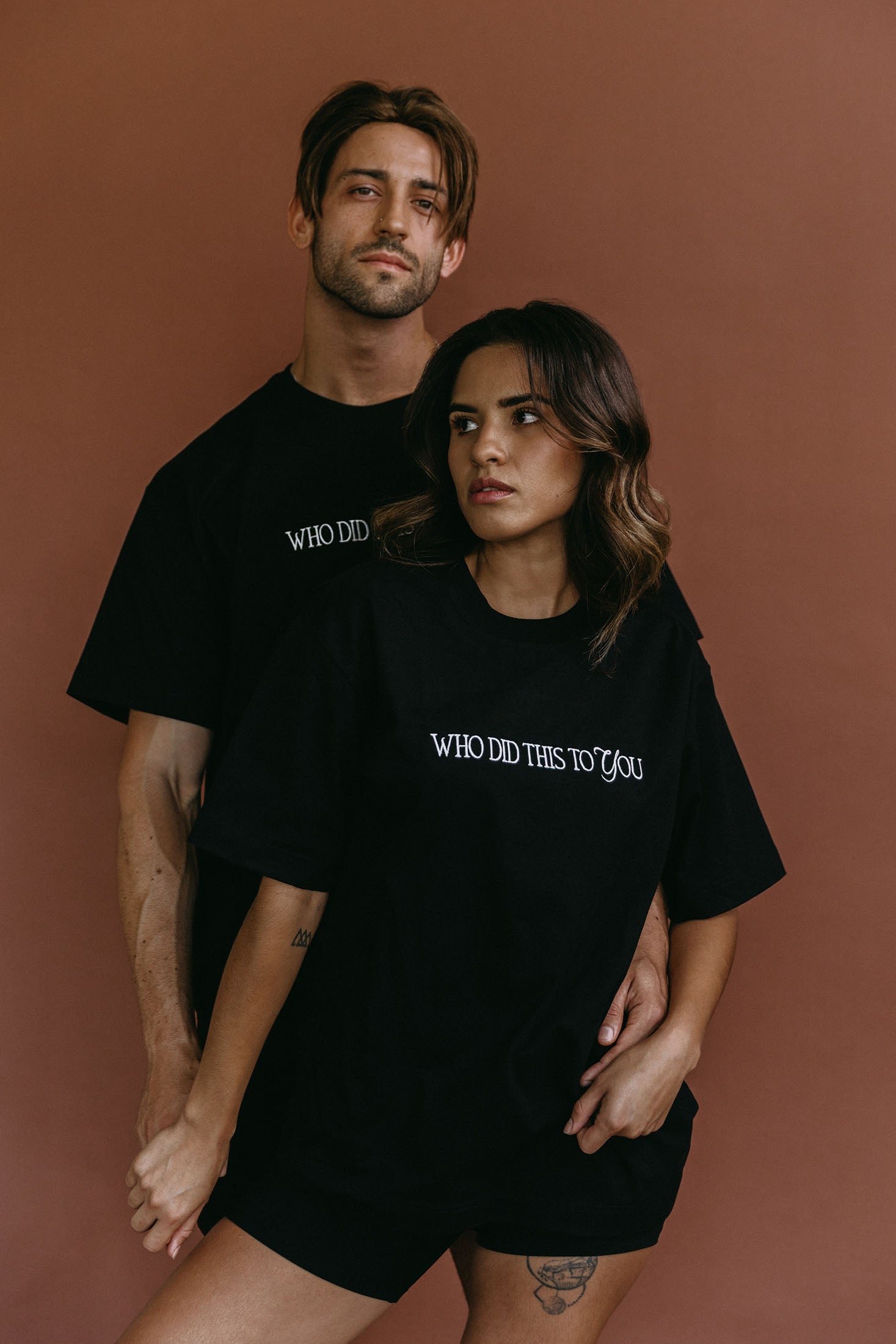 Couple wearing the black "Who Did This To You" relaxed fit embroidered T-shirt by WNGSPN, styled as elevated romance reader apparel.