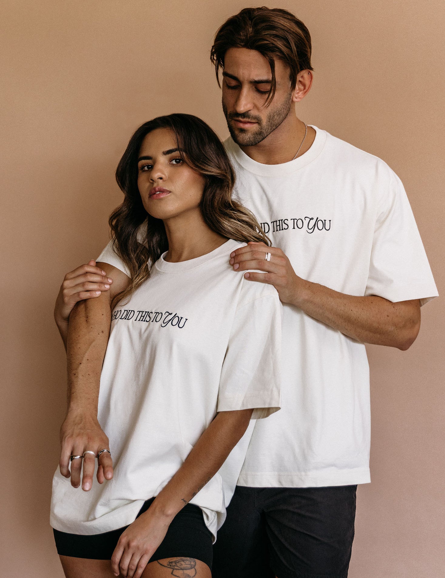 Couple wearing the ecru "Who Did This To You" relaxed fit embroidered T-shirt by WNGSPN, capturing a refined bookish aesthetic.