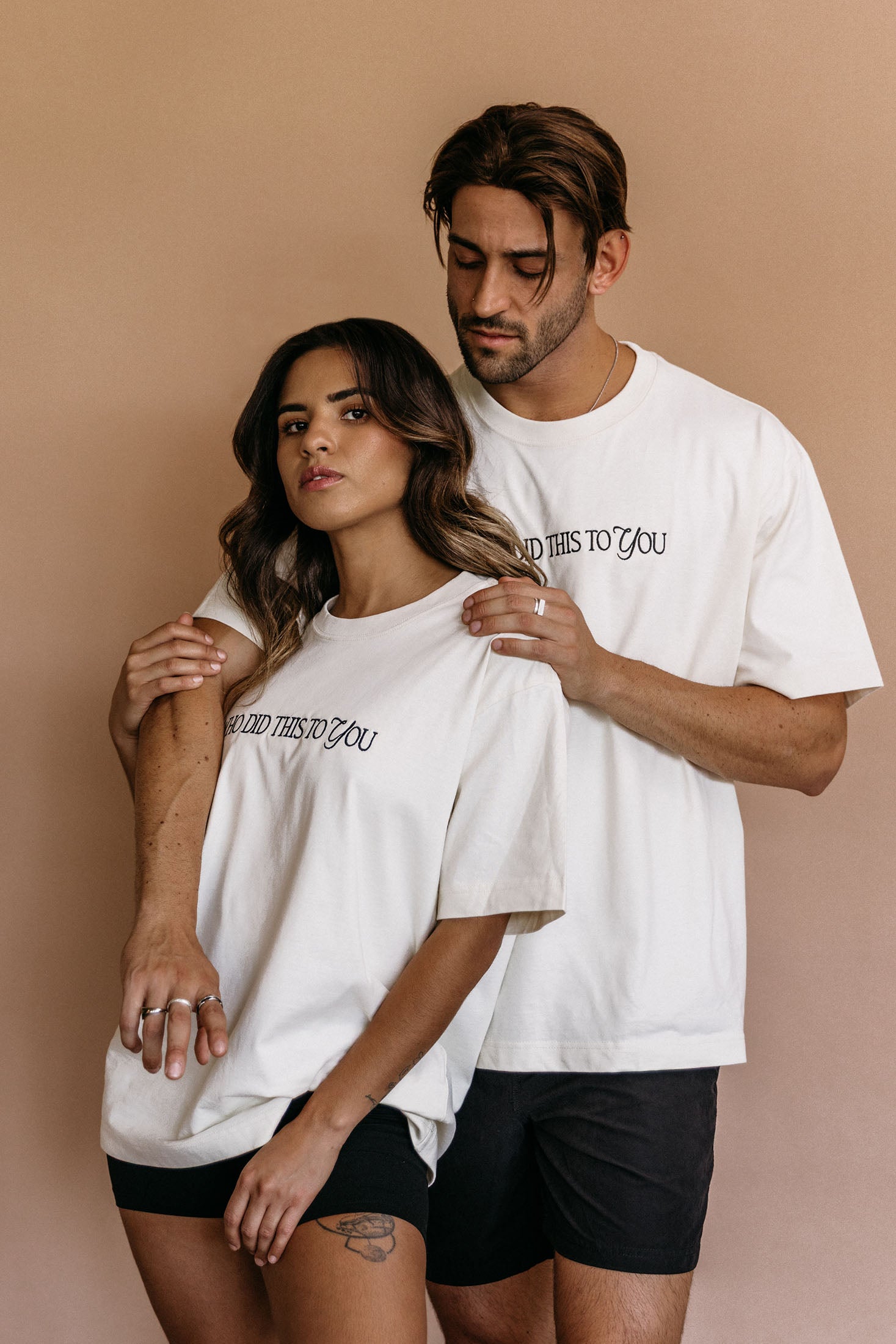 Couple wearing the ecru "Who Did This To You" relaxed fit embroidered T-shirt by WNGSPN, capturing a refined bookish aesthetic.