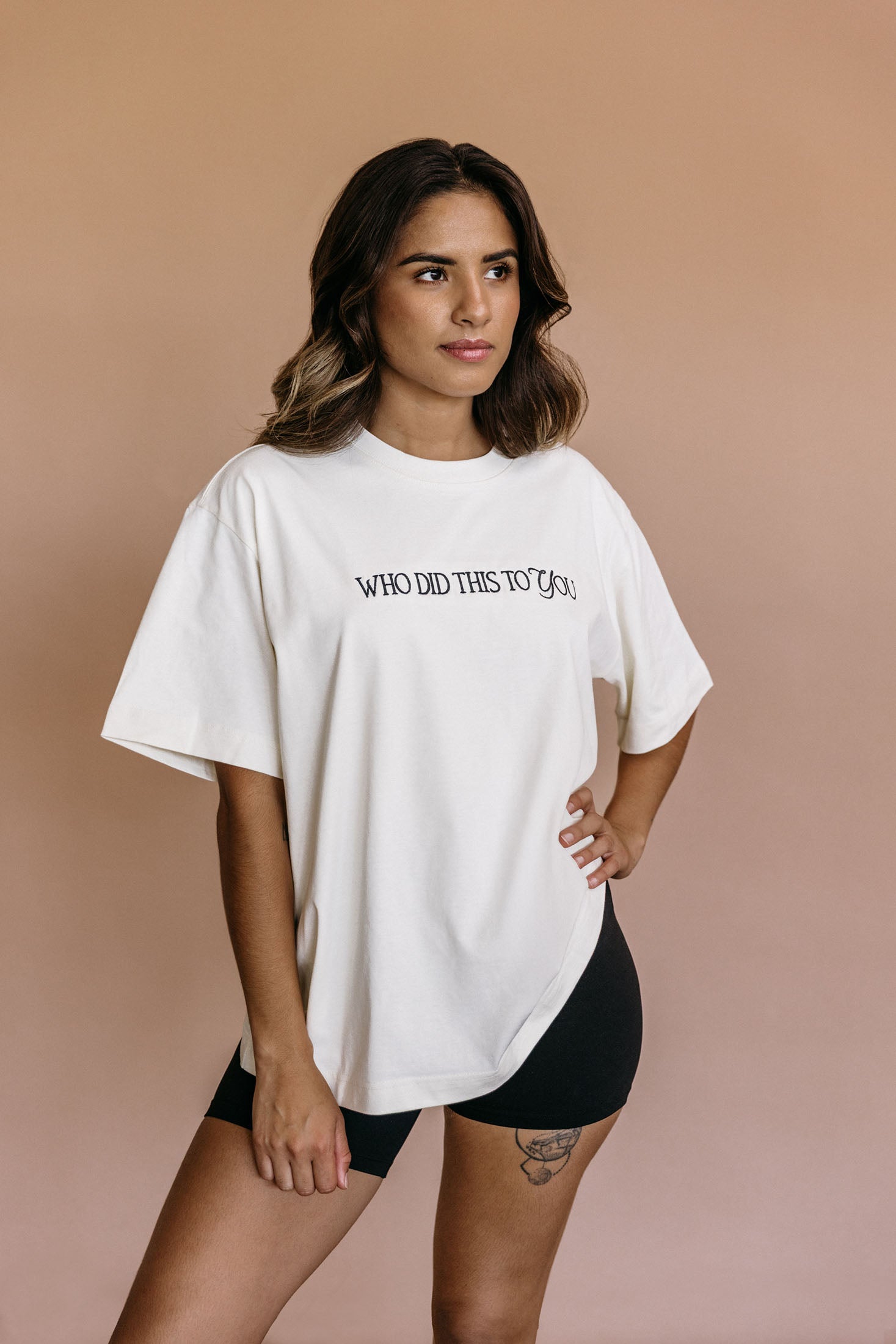 Female model wearing the ecru "Who Did This To You" relaxed fit embroidered T-shirt by WNGSPN, styled in a minimal, elevated aesthetic.