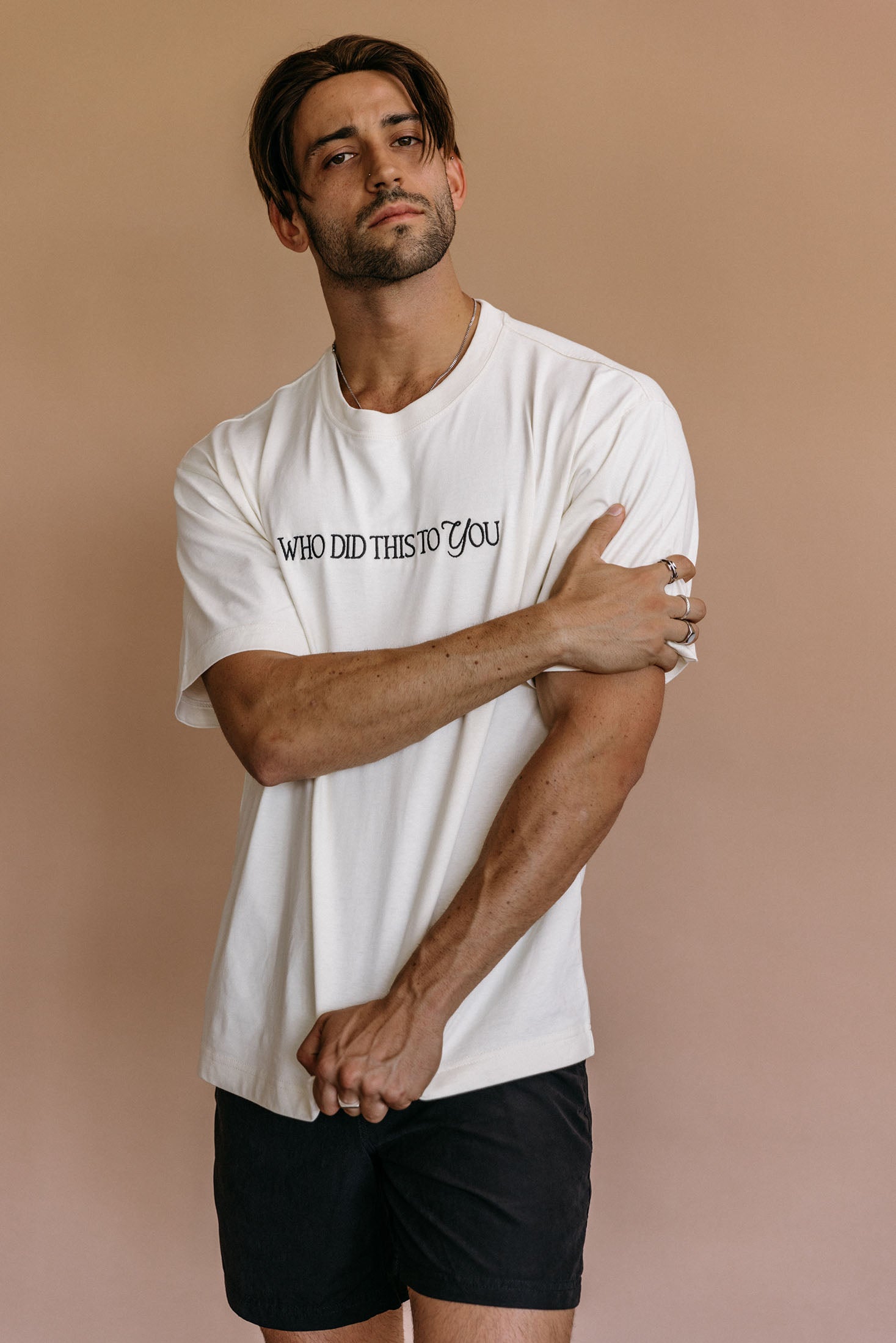 Male model wearing the ecru "Who Did This To You" relaxed fit embroidered T-shirt by WNGSPN, styled in a minimal, elevated aesthetic.