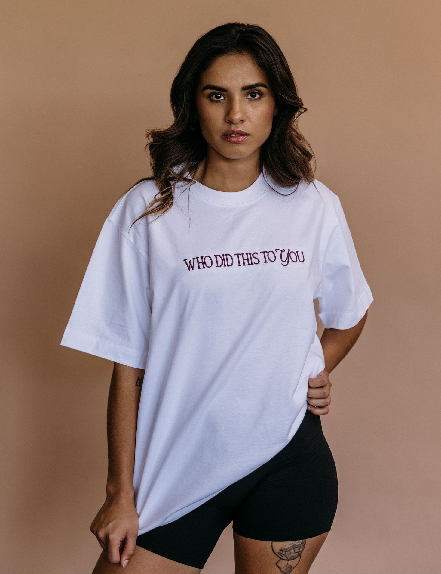 Female model wearing the ecru "Who Did This To You" relaxed fit embroidered T-shirt by WNGSPN, styled in a minimal, elevated aesthetic.