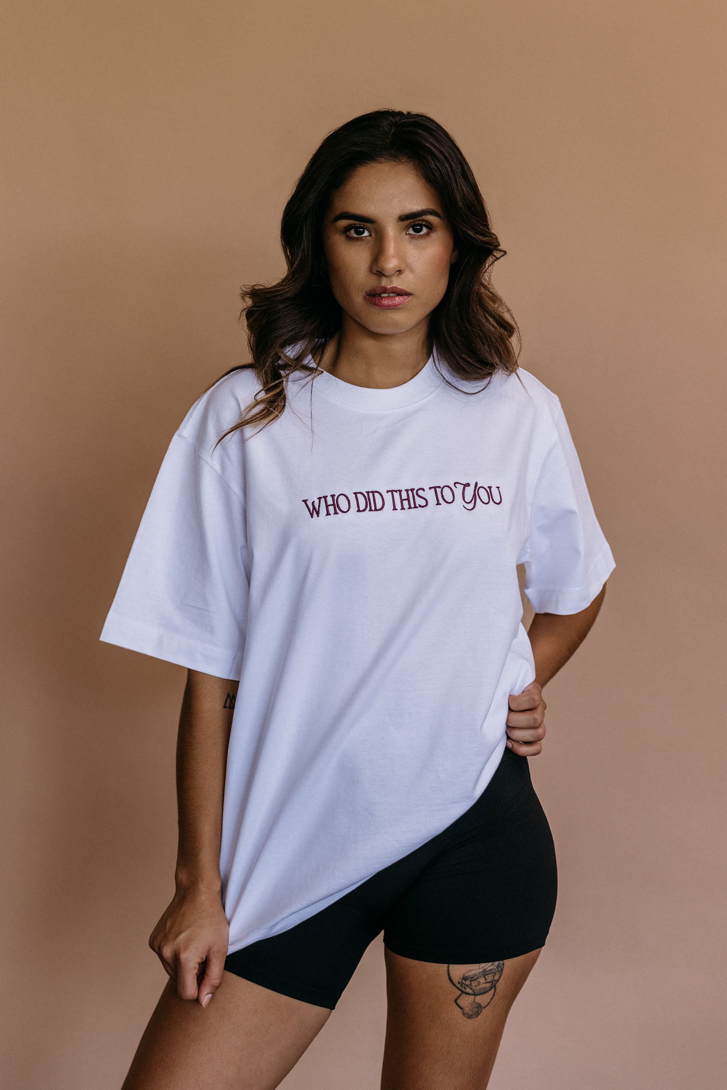 Female model wearing the ecru "Who Did This To You" relaxed fit embroidered T-shirt by WNGSPN, styled in a minimal, elevated aesthetic.