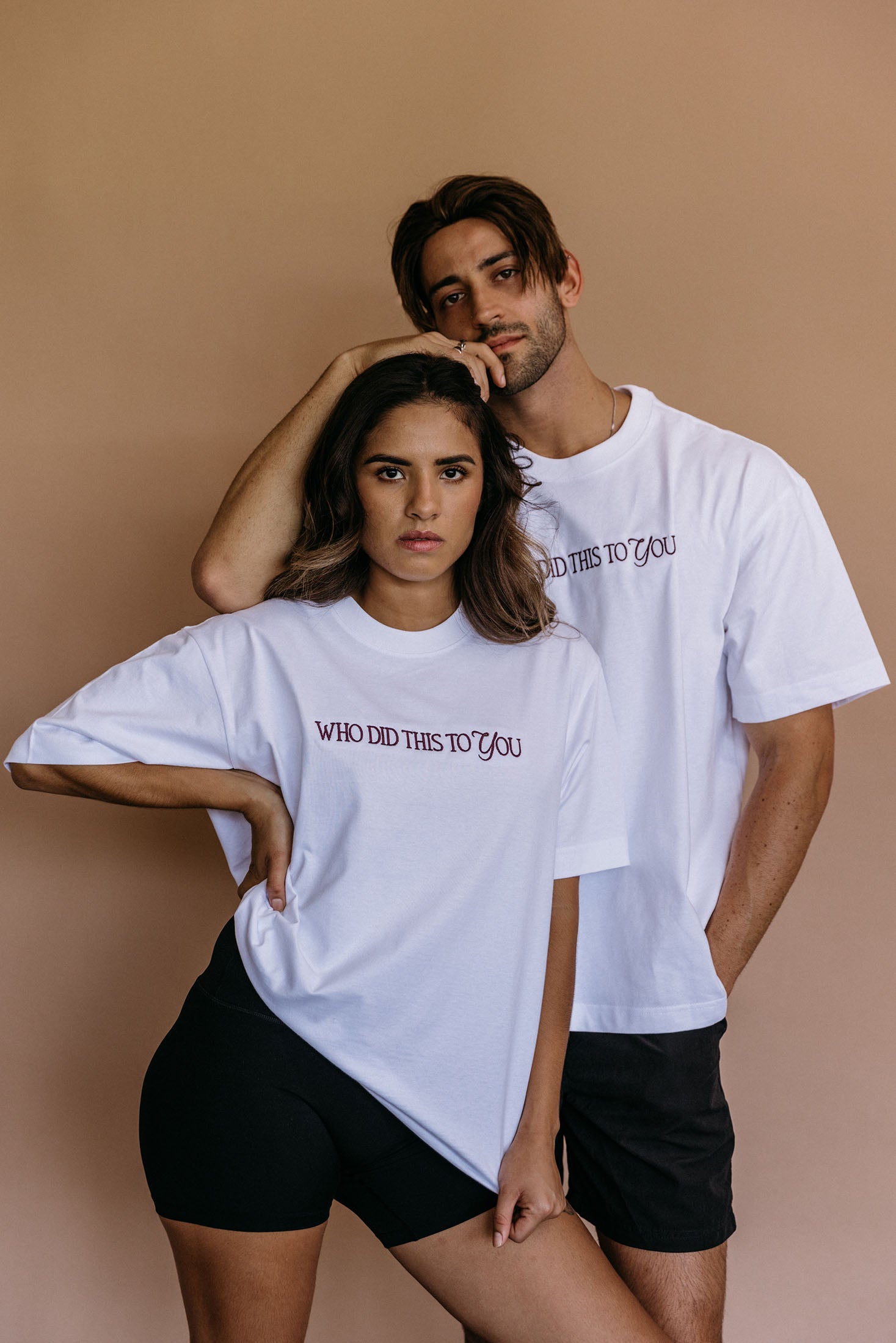 Couple wearing the white "Who Did This To You" relaxed fit embroidered T-shirt by WNGSPN, with subtle tension and modern edge.